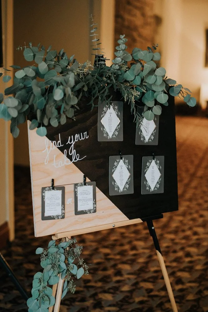 A  black and natural wooden board decorated with greenery holding the seating chart at the Alderbrook Resort-Photography by Nick plus Danee Photography.-planned and designed by Simply Wed