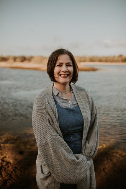 Portrait of Clare. Clare is smiling, looking friendly. Clare is standing in front of a lake in the Netherlands.