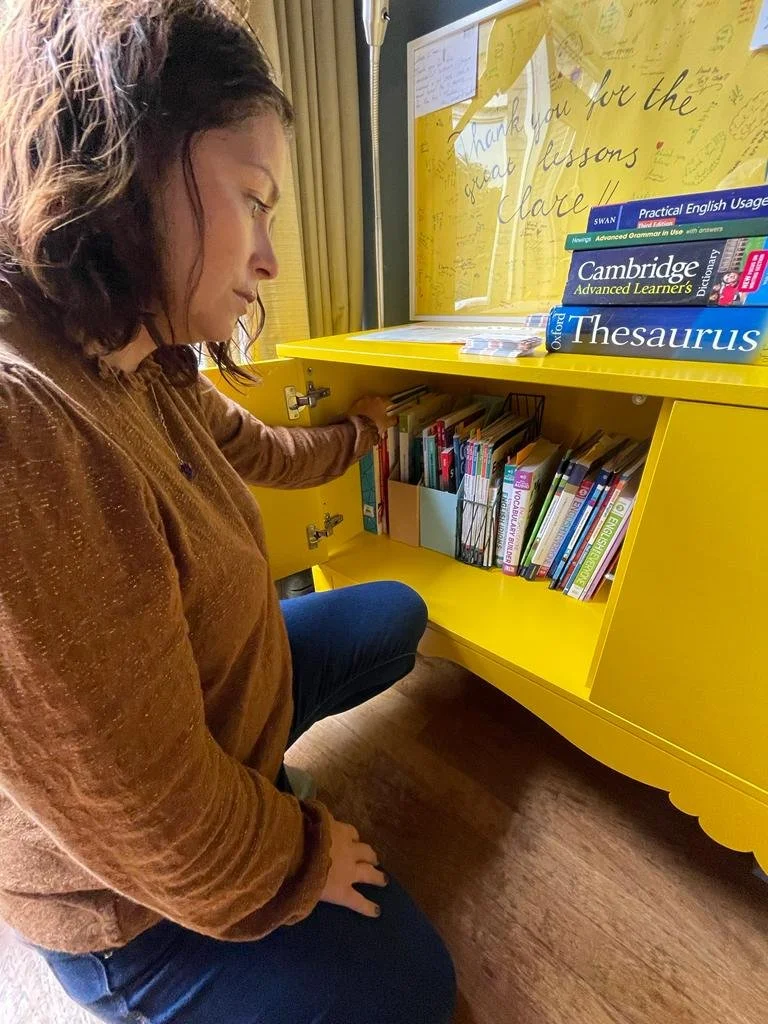 Clare a female english teaching is looking through her cupboards to find an english grammar book
