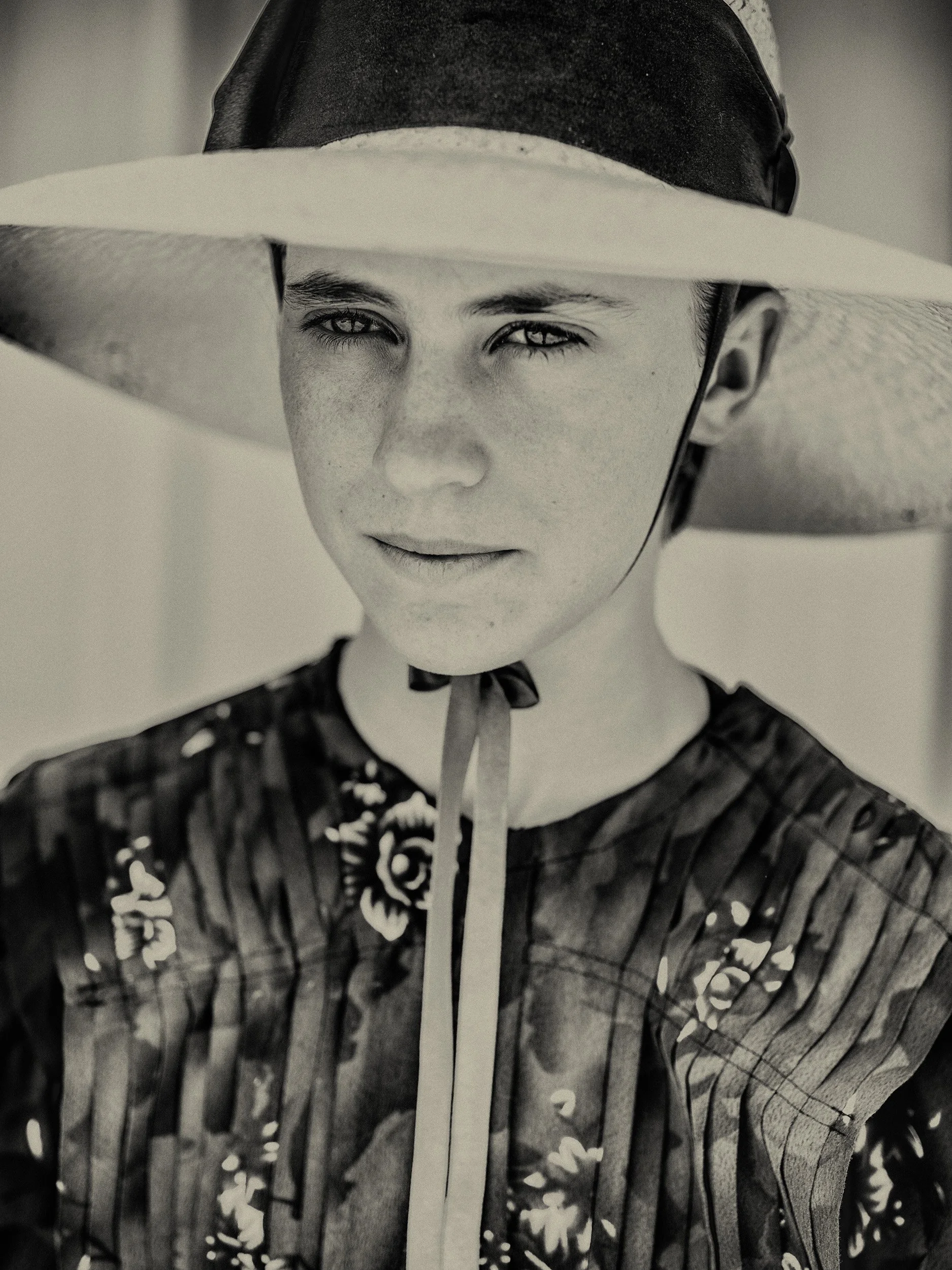 Een jonge vrouw met een hoed draagt een bloemenjurk en kijkt in de verte.