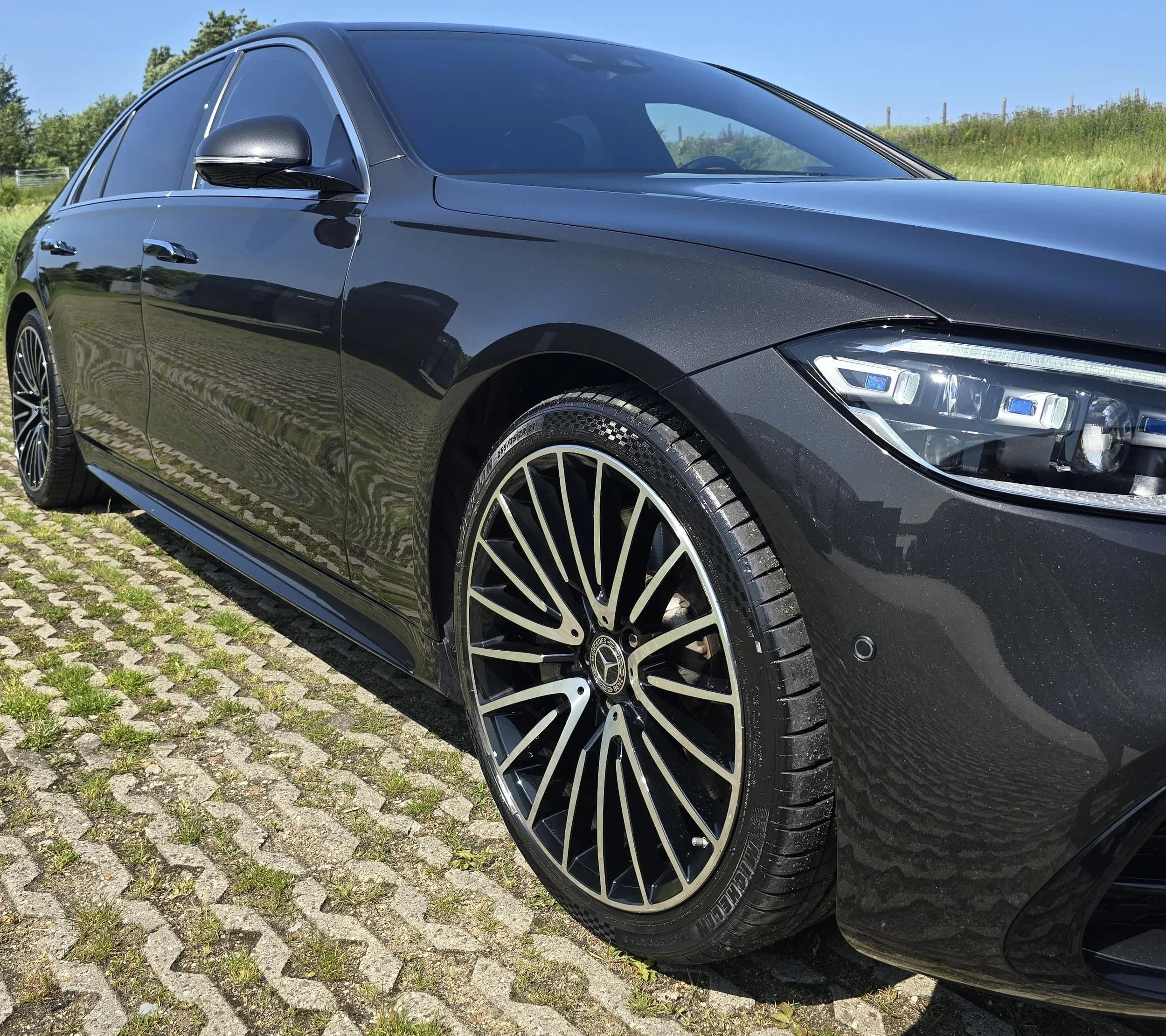 Zwarte Mercedes-Benz sedan geparkeerd op een grindpad op een zonnige dag.