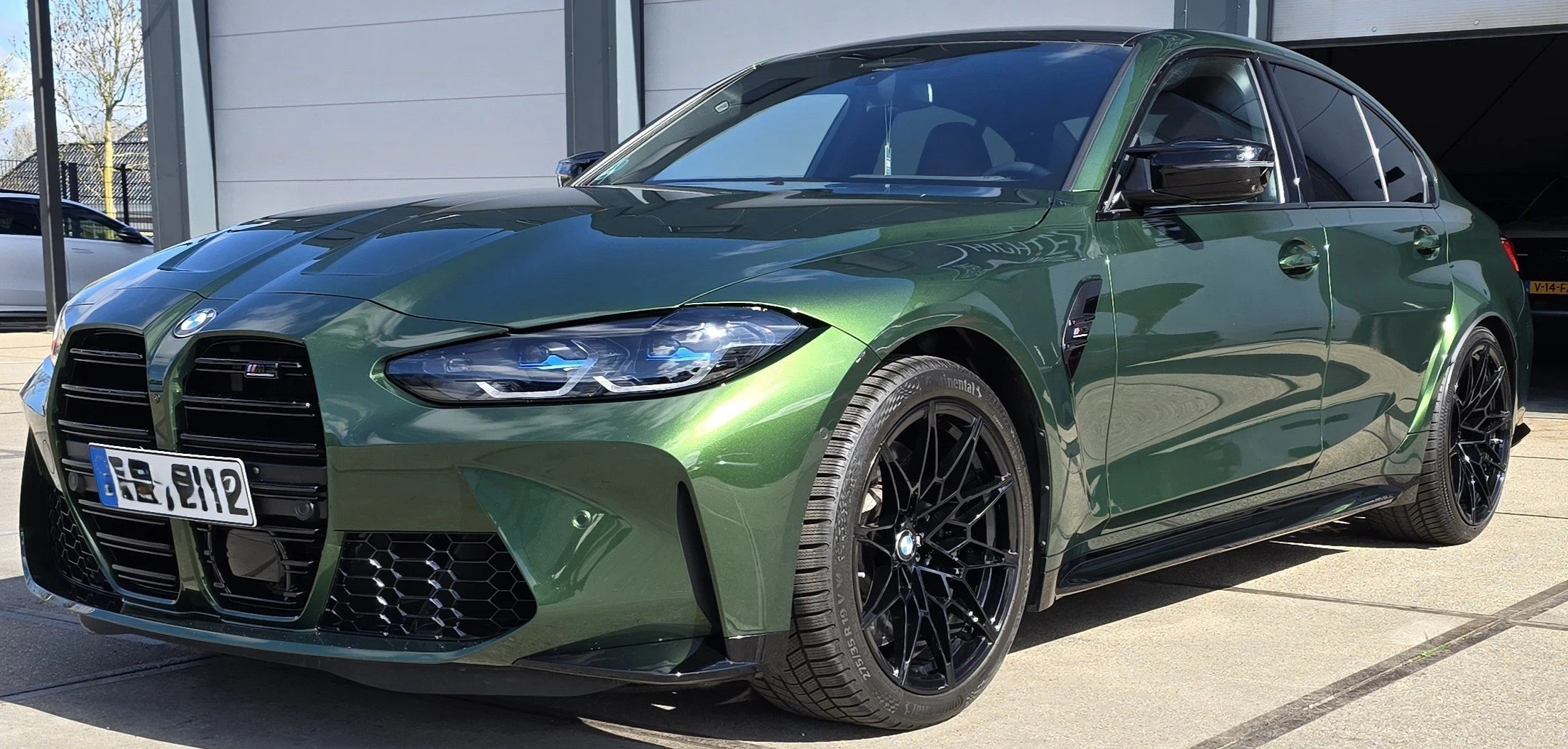 Groene BMW M3 auto met zwart lichtmetalen velgen geparkeerd buiten.