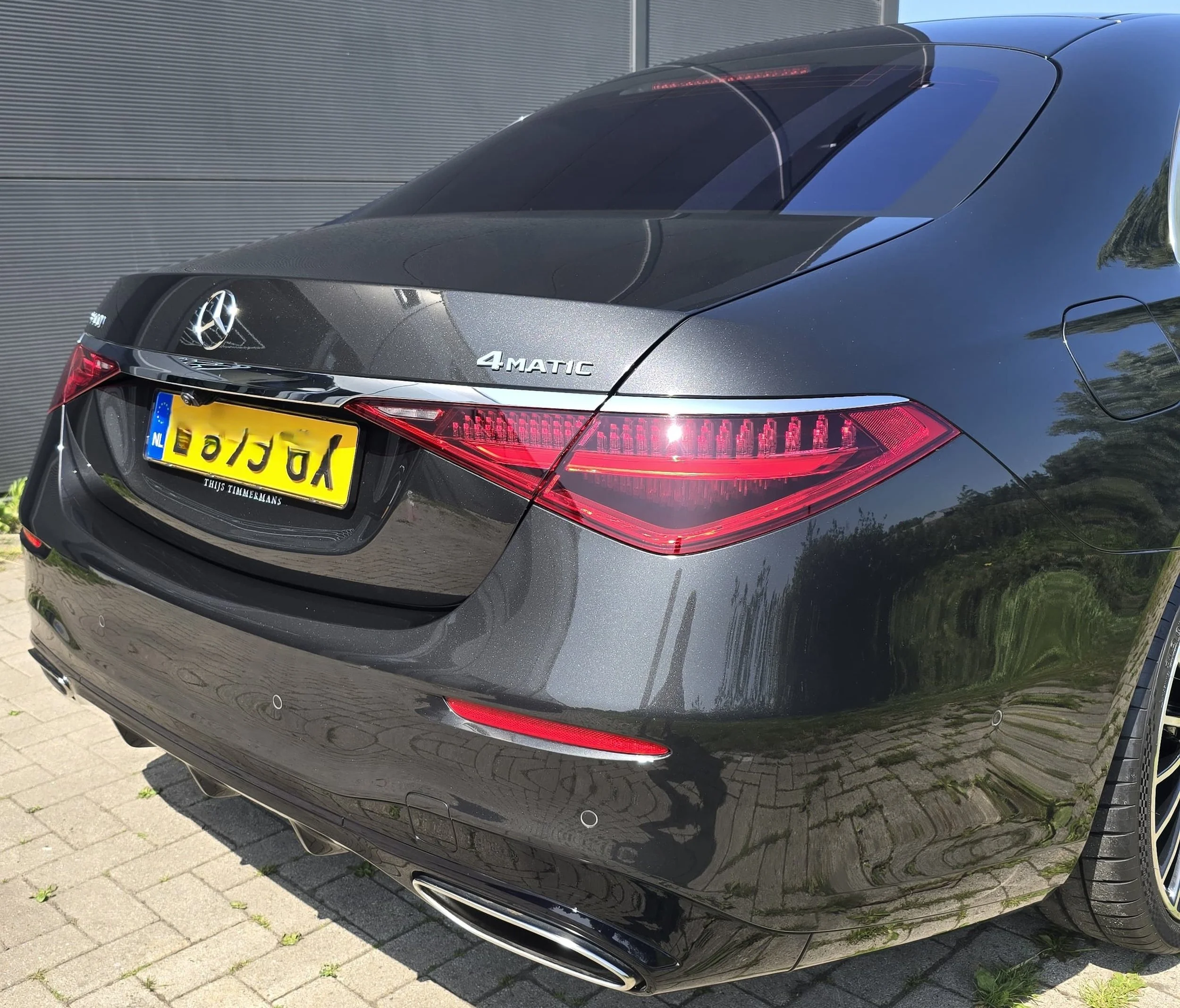 De achterkant van een zwarte Mercedes-Benz auto met een registerplaat en badge, parked op een straat met stenen tegels.