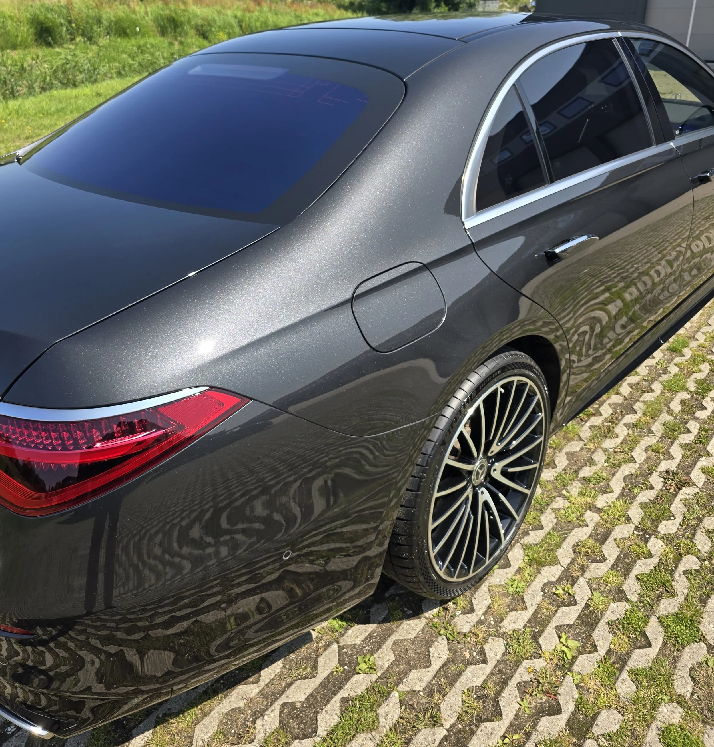 Zwarte luxe sedan auto geparkeerd op een stenen oprit, met sportvelgen en spatten van zonlicht op de lak.