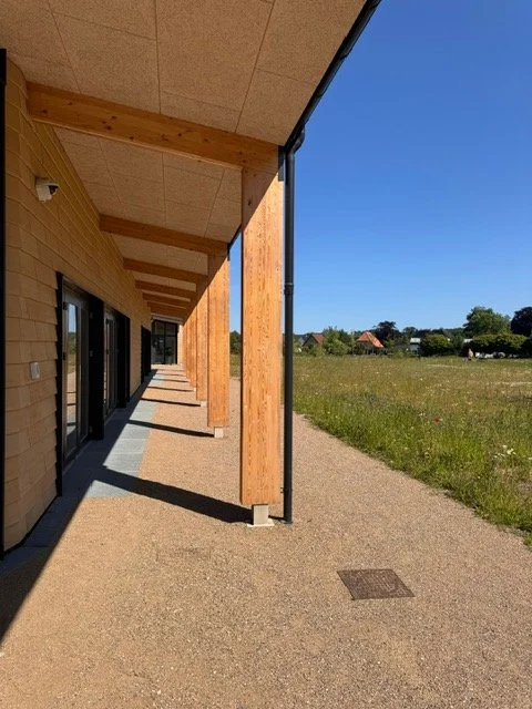 Udendørs veranda med træbjælker og udkig over et grønt landskab under en klar blå himmel.
