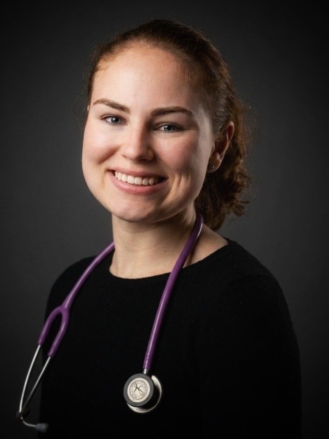 Portrait of a smiling female healthcare professional with a stethoscope around her neck, wearing a black top.