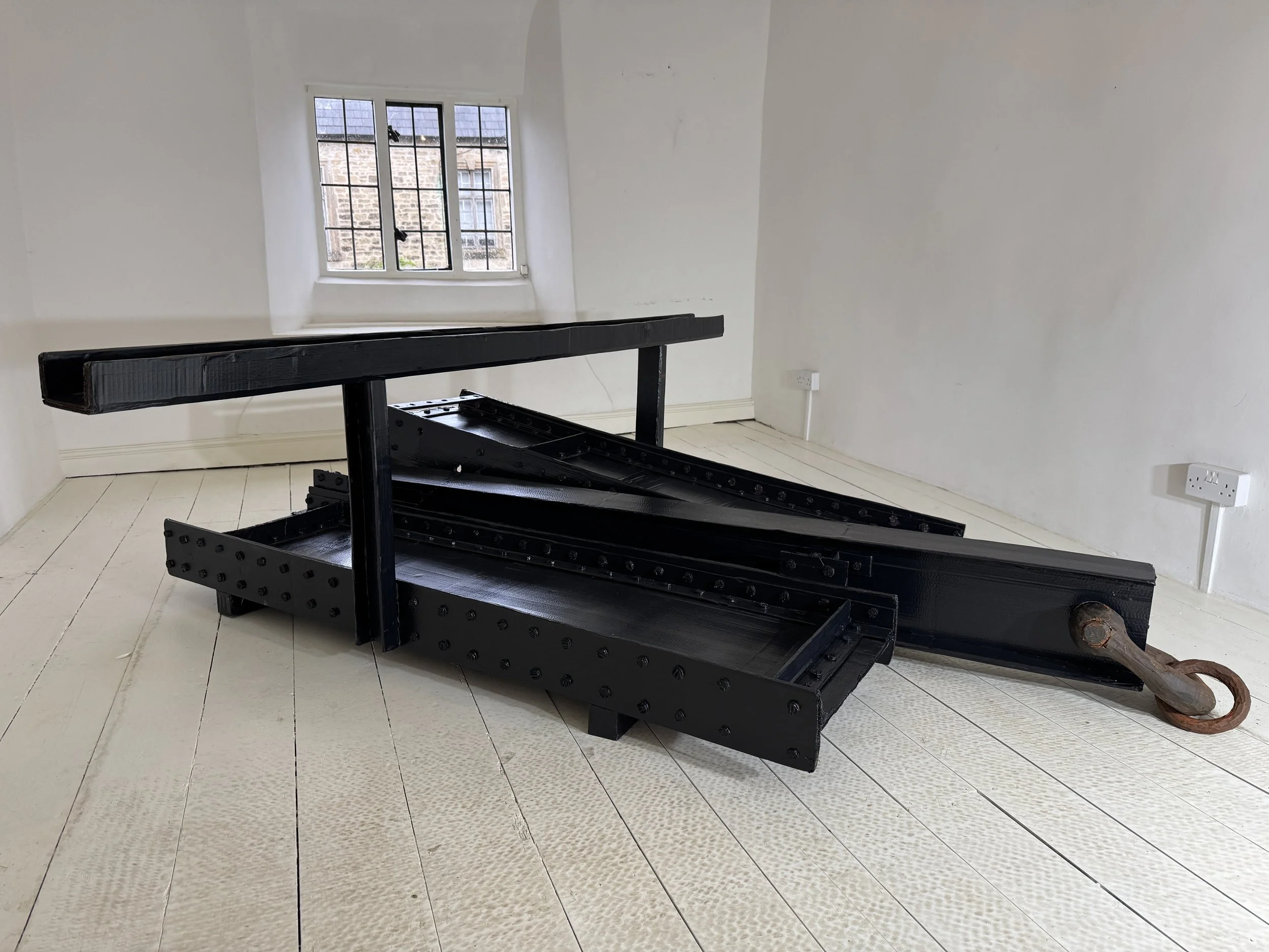 Very dark navy blue painted cardboard sculpture in a white painted domestic cottage bedroom; the form resembles Anthony Caro's work, with the addition of a brown painted cardboard shackle 