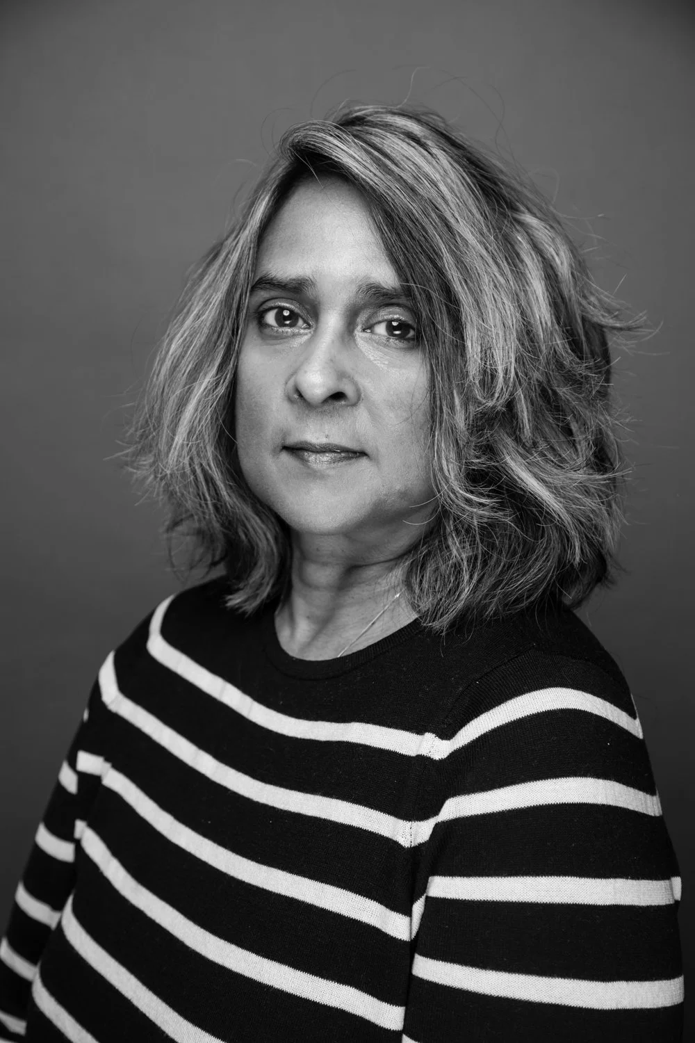 Black and white portrait of a woman with shoulder-length, wavy hair wearing a striped shirt.
