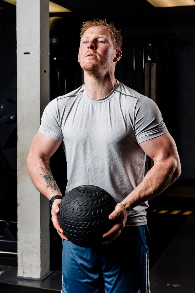 A man in workout attire holding a black medicine ball in a gym.