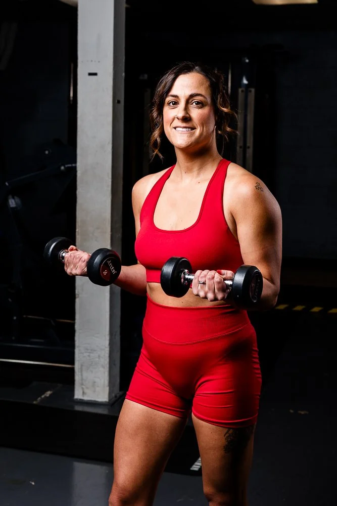 Woman in red sports bra and shorts lifting dumbbells indoors in gym.