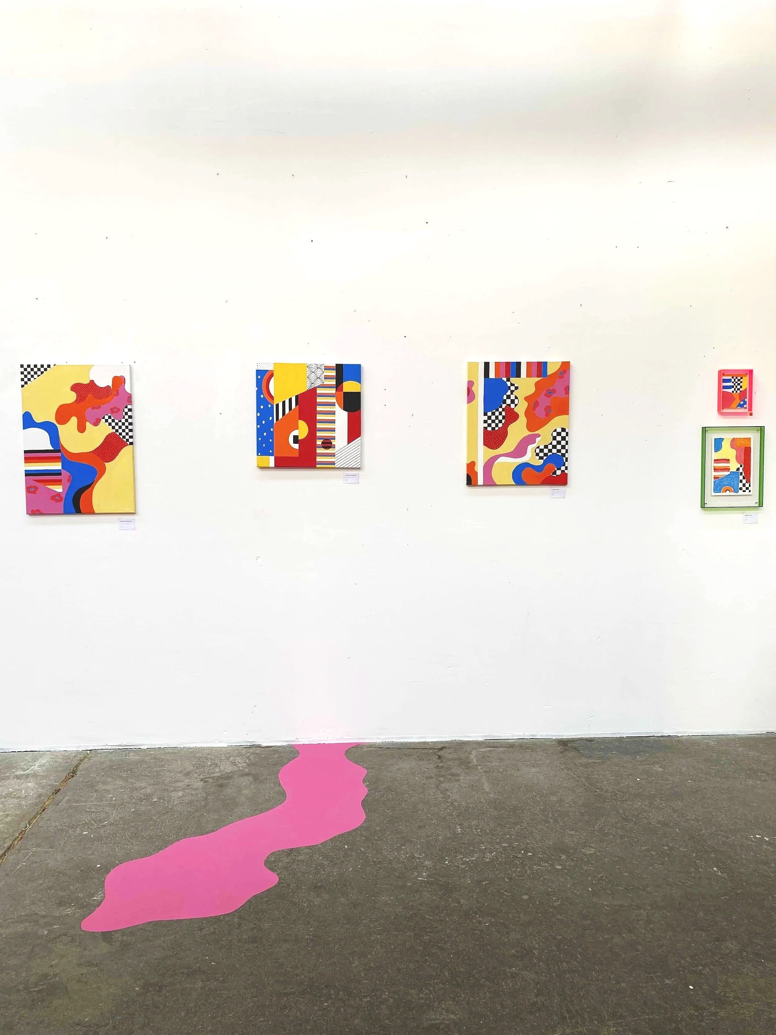 Exposition de cinq œuvres d'art colorées et abstraites accrochées à un mur blanc, avec une traînée rose sur le sol.