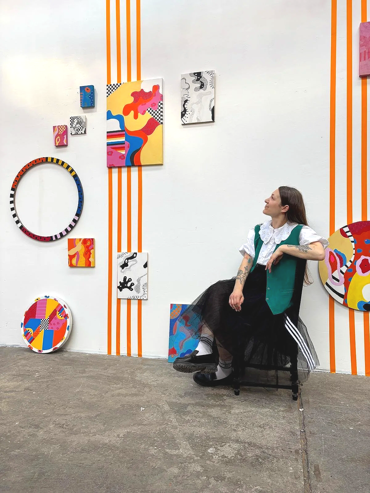 Amande assise regardant ses tableaux au mur pendant son exposition.