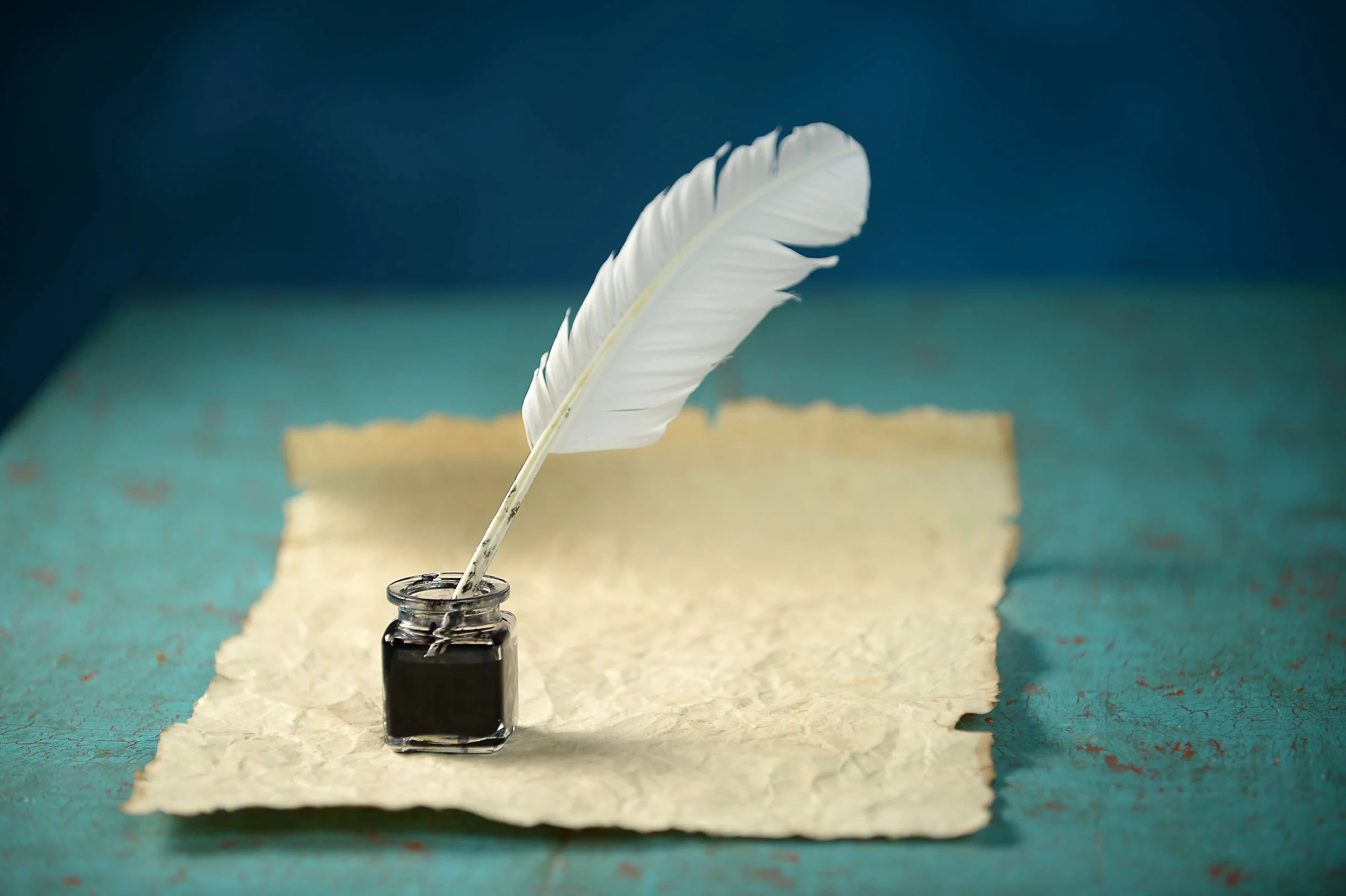 Quill pen dipped in ink bottle with parchment paper on a textured table.