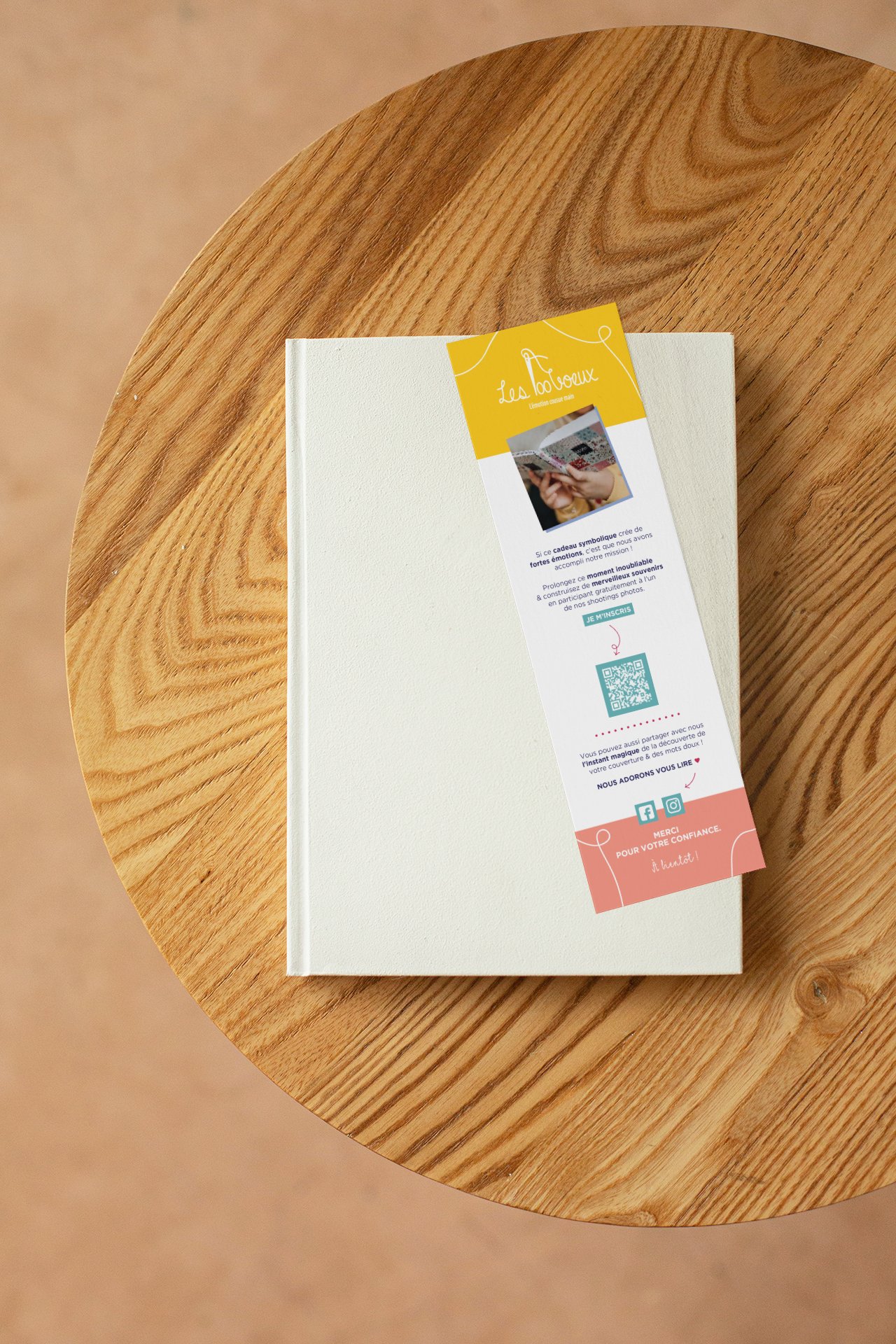 Livre blanc avec un marque-page ludique promotionnel créé pour Les 100 Vœux posé sur une table ronde en bois.