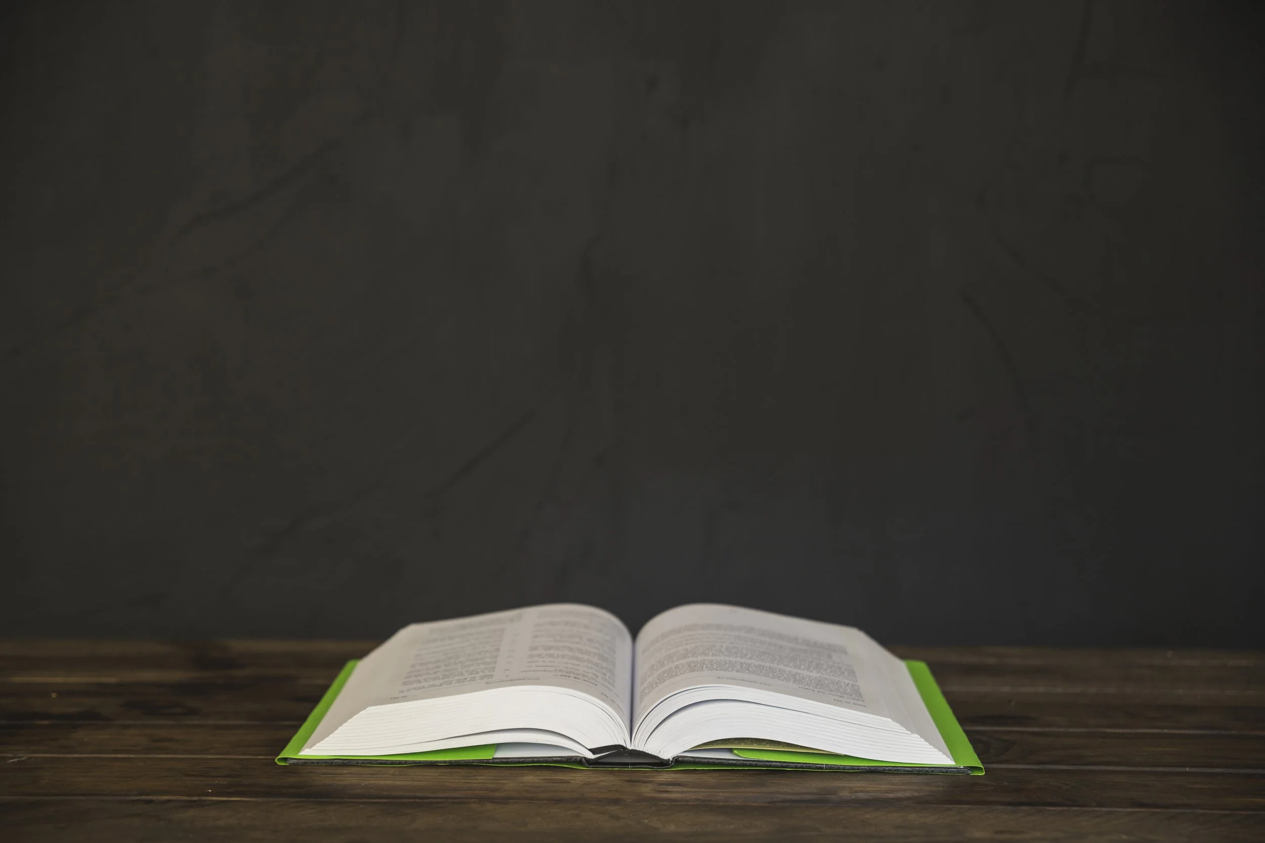 An open book with a green cover on a wooden table against a dark background.