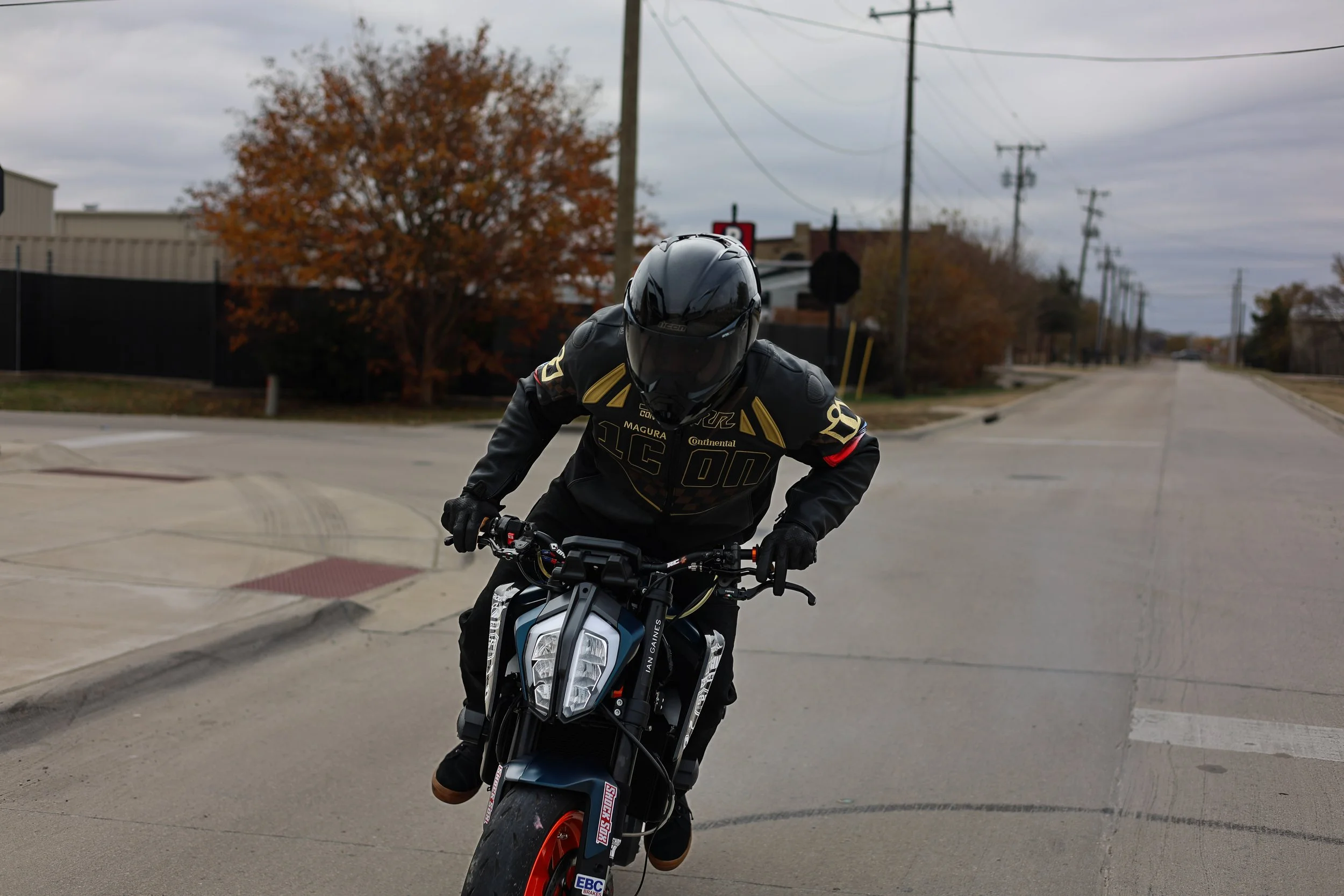 A person riding a black and orange KTM motorcycle on a residential street with overcast skies