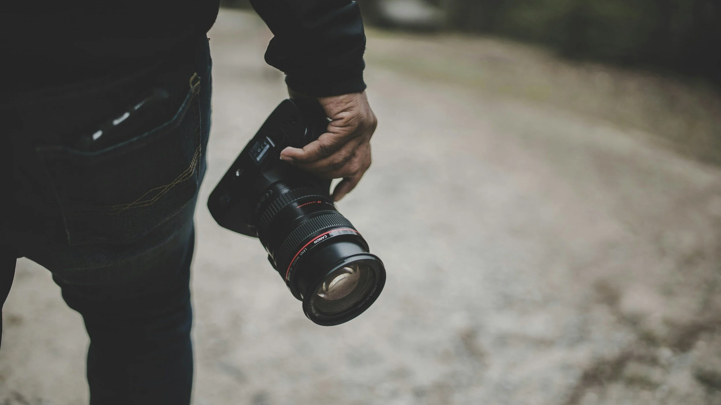 Close-up of a person holding a professional camera with a large lens in an outdoor setting.