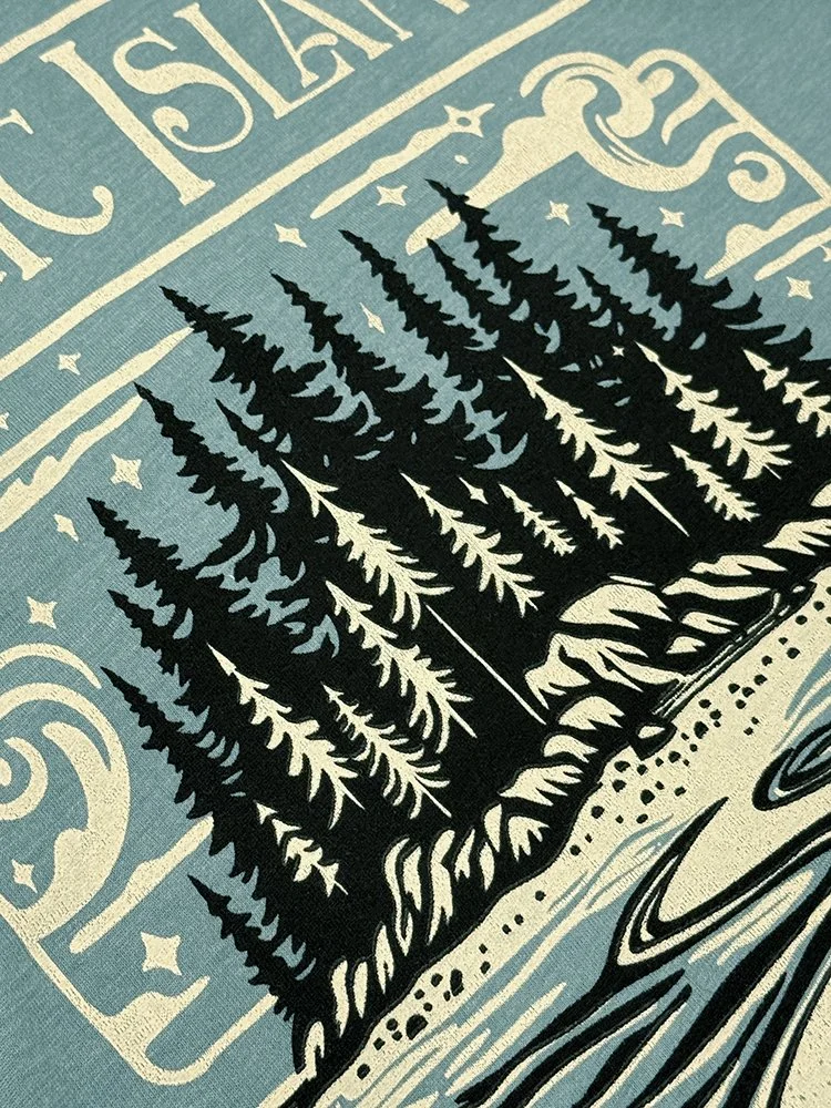 Close-up of the two-color Magic Island design showing black and creamy white ink on the soft blue fabric.