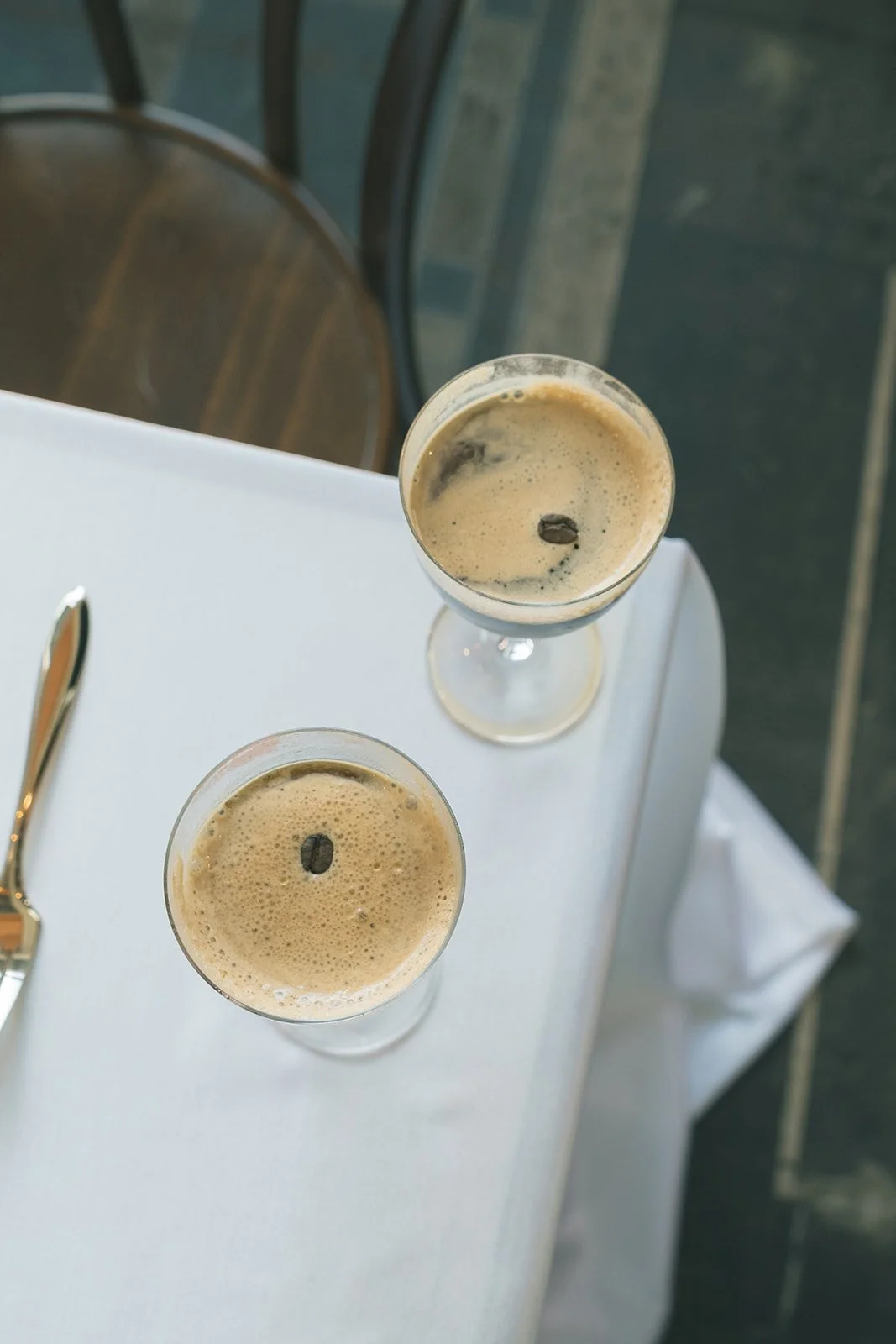 Two espresso martinis sitting on top of a table with a white table cloth.