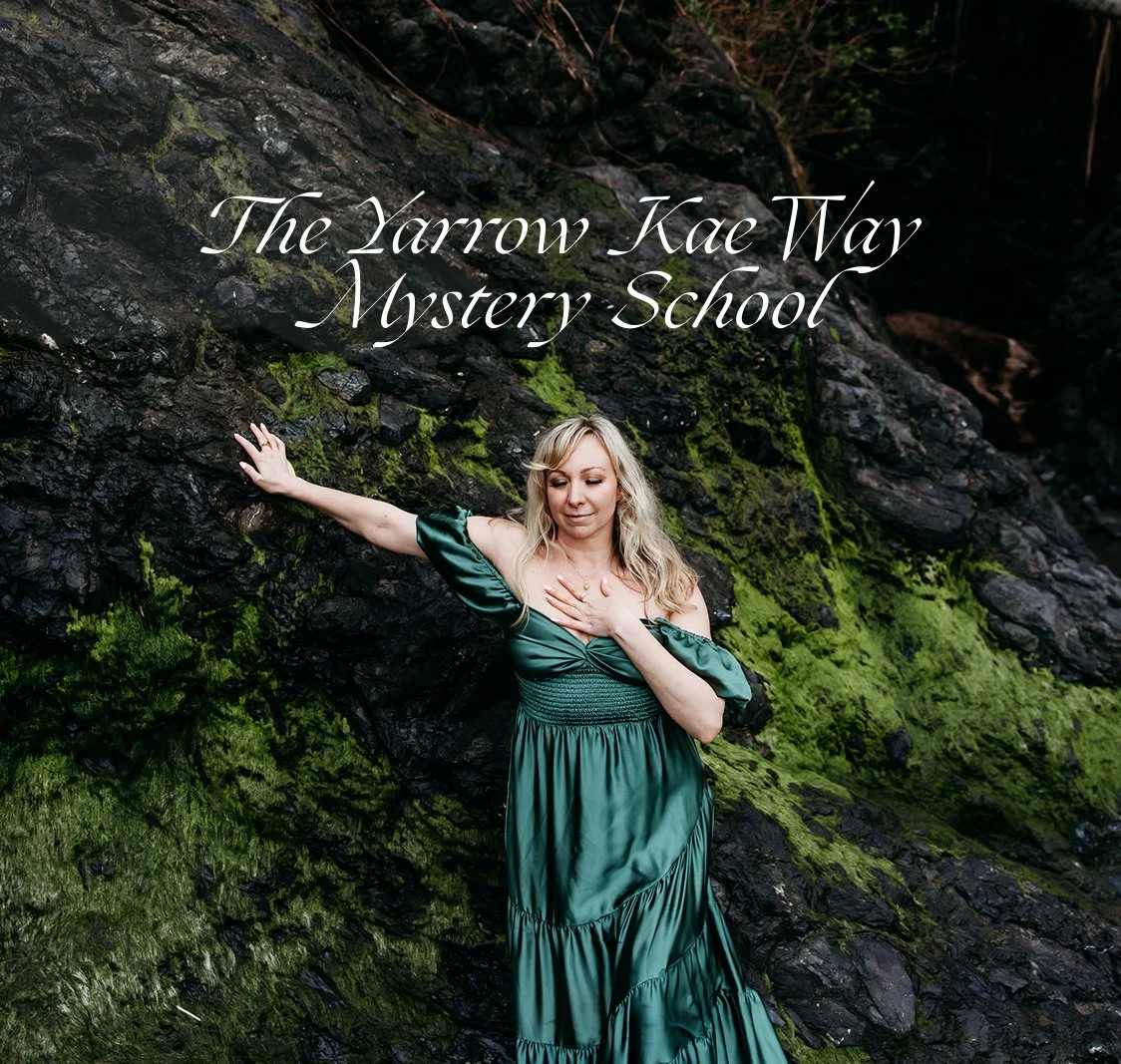 A woman in a green dress leaning against moss-covered rocks with the text 'The Yarrow Kae Way Mystery School' overlaid.