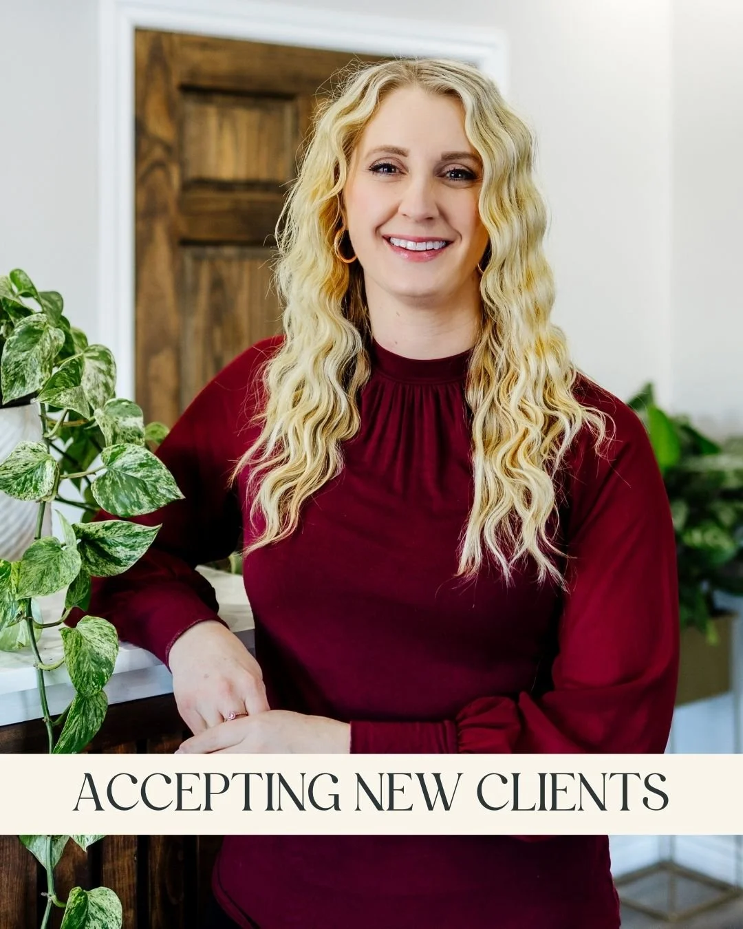 Anita Gemill, RSW, MSW - A smiling woman with wavy blonde hair wearing a burgundy top, and leaning on a wooden counter with a green leafy plant nearby and a caption that reads "Accepting New Clients."