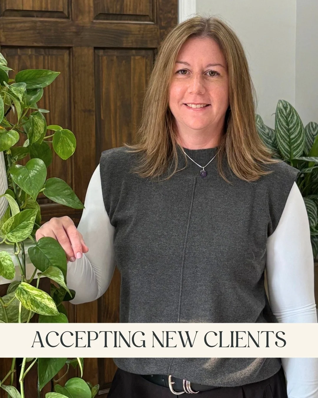 Laura Wood, RP (Qualifying) - A smiling woman with brown hair, wearing a gray vest and white long-sleeve shirt, and leaning on a wooden counter with a green leafy plant nearby and a caption that reads "Low-Cost Therapy, Accepting New Clients
