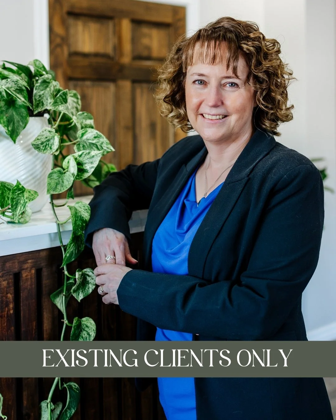 Jennifer Cox, MSW, RSW - A smiling woman with curly hair wearing a black blazer and blue top, and leaning on a wooden counter with a green leafy plant nearby and a caption that reads "Currently Unavailable."