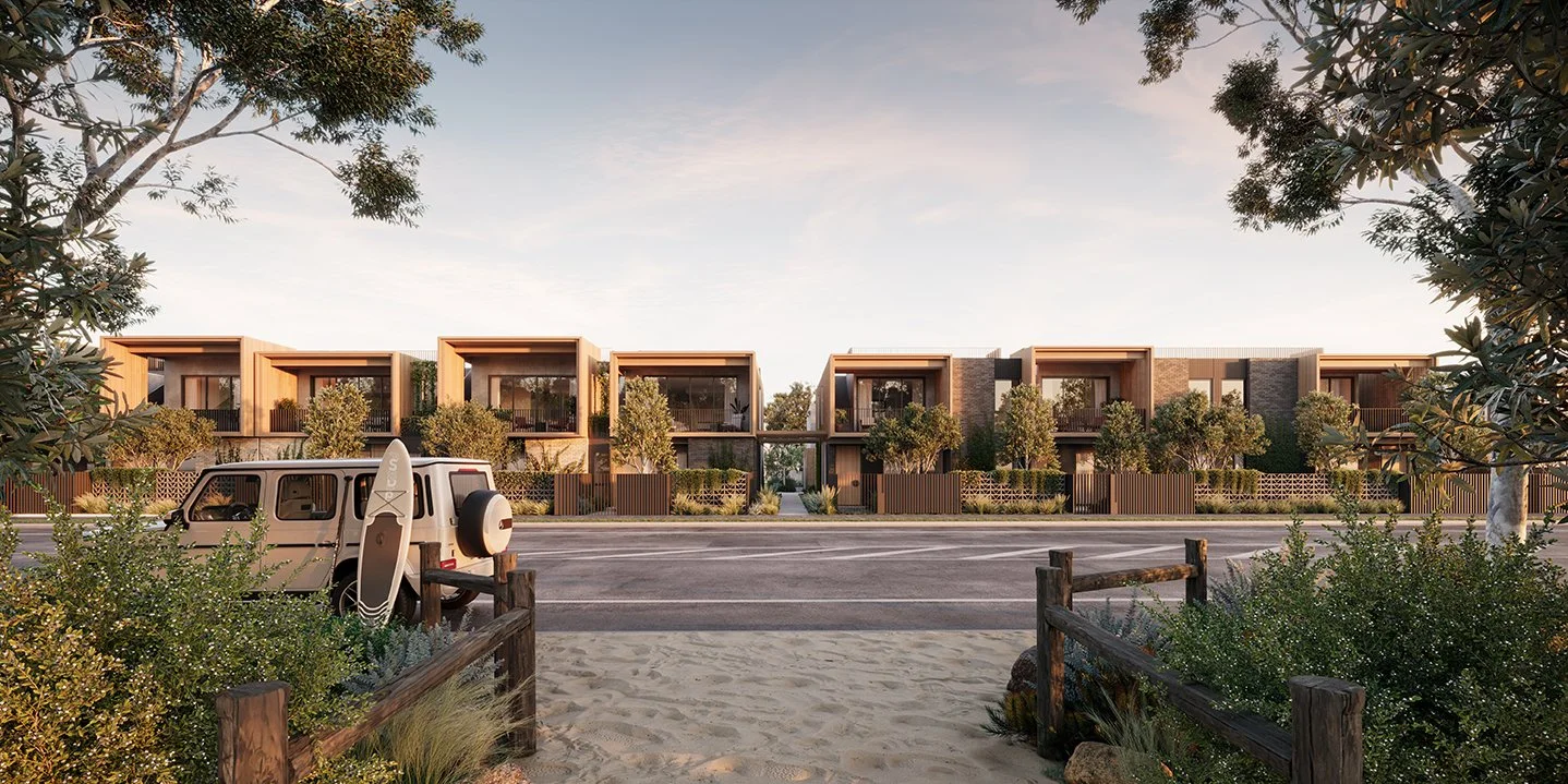 Modern row of townhouses with large windows and balconies, surrounded by trees and greenery, viewed from a sandy foreground with a parked vehicle and surfboards in front.