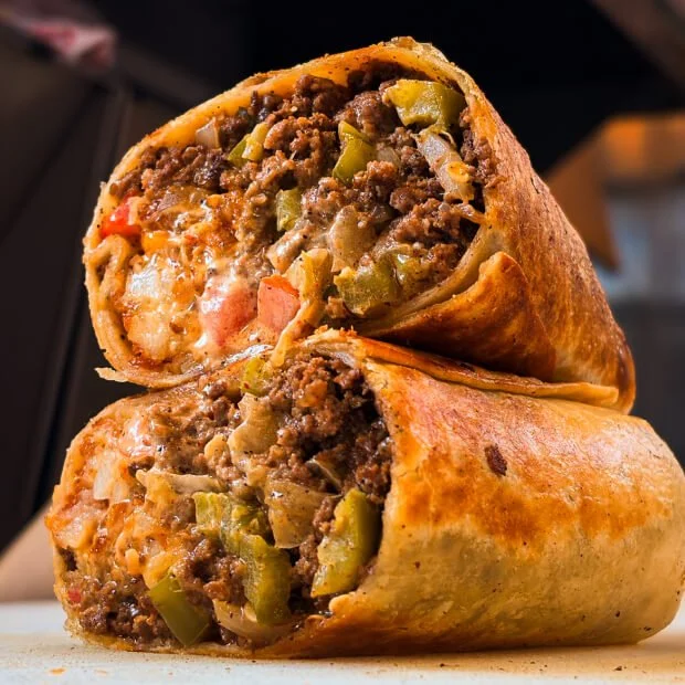 Cross-section of a beef and vegetable burrito with ground beef, diced tomatoes, green peppers, onions, and cheese in a flour tortilla