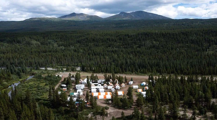 A small campground with tents surrounded by dense forest and mountains in the background.