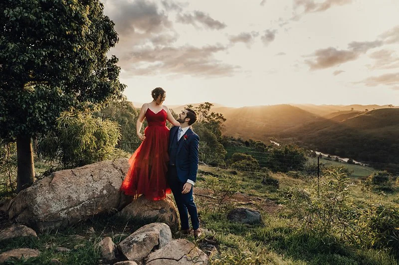 A stunning red wedding dress standing up on the rocks in the sunset at Brindabella Hills winery Canberra. Canberra's top wedding photographer.