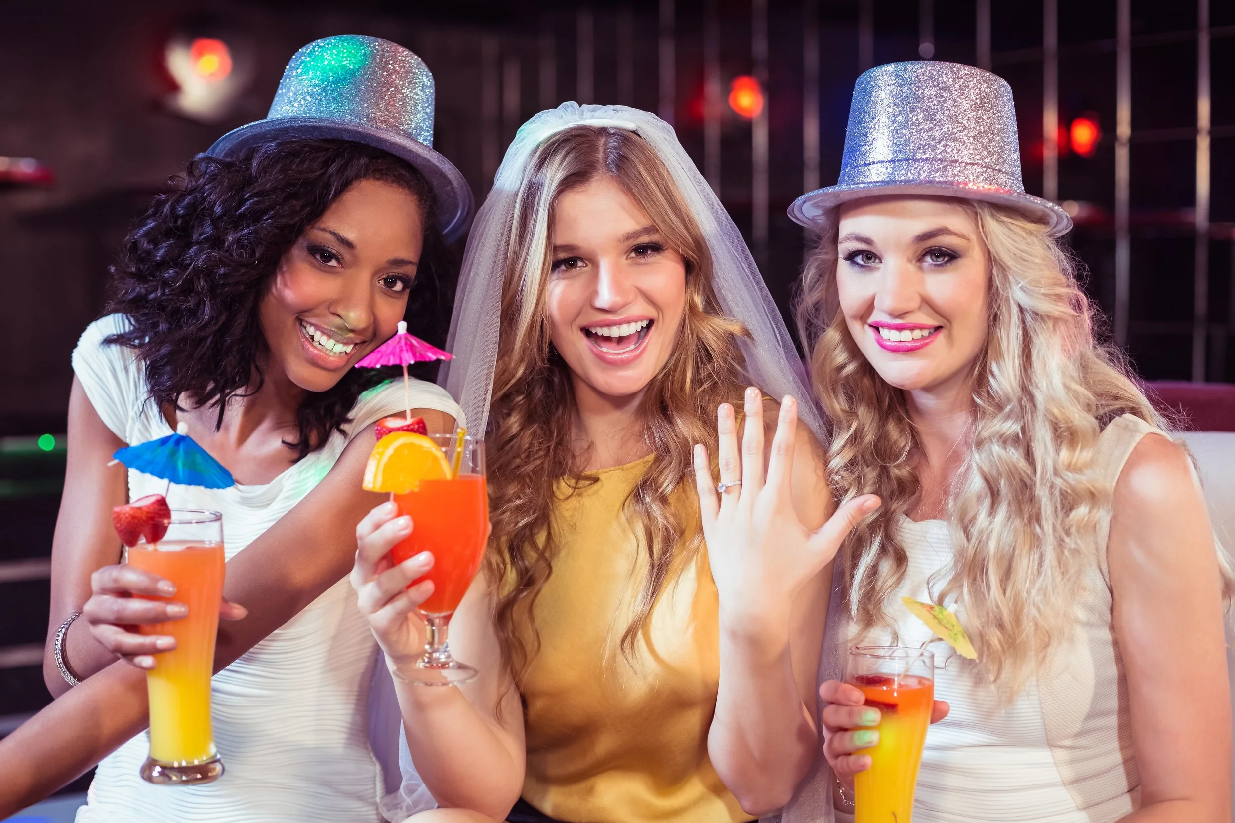 Three ladies with hen do props, middle lady showing engagement ring