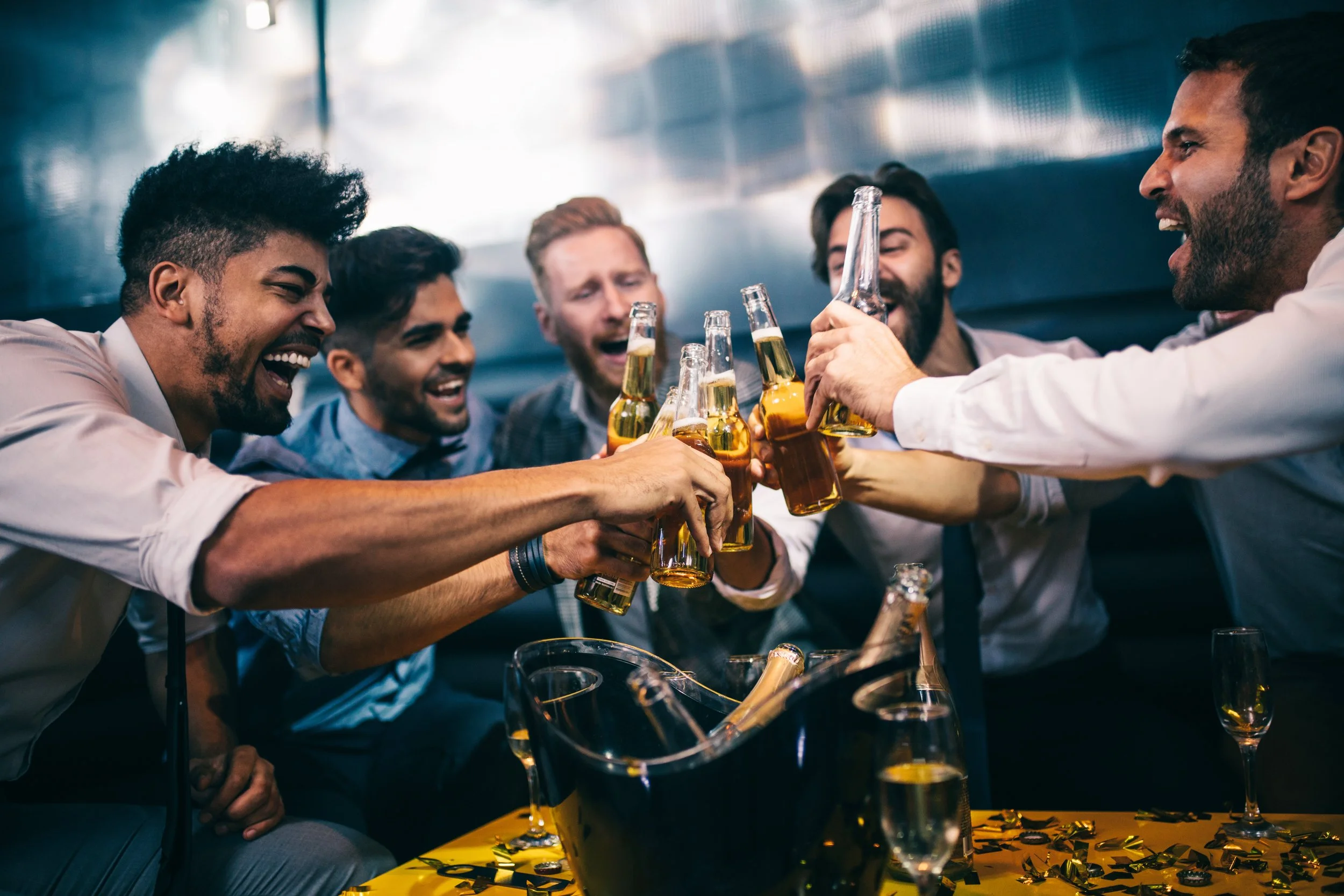 Group of men celebrating and cheers'ing with glass beer bottles