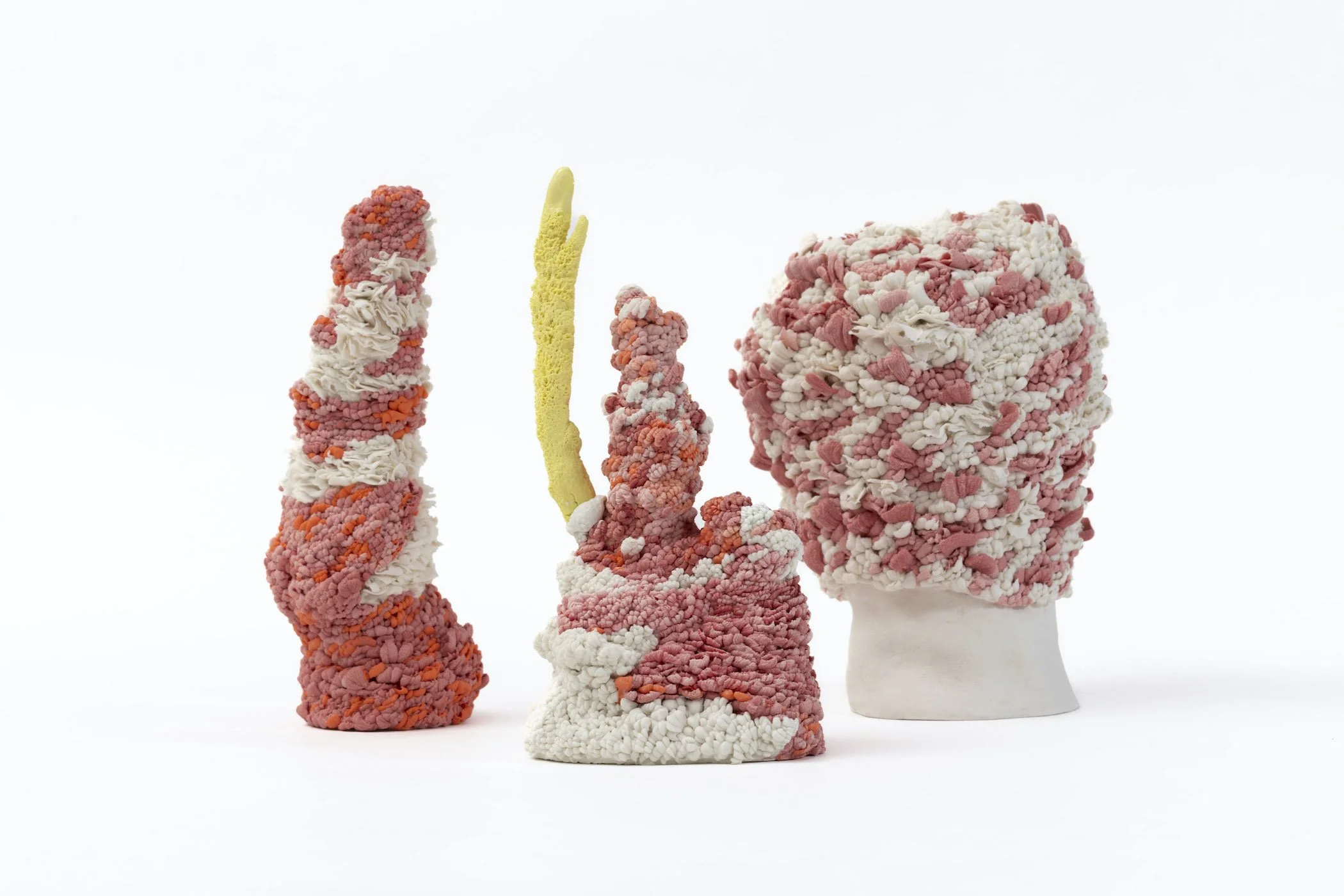 Installation of three hand-built porcelain sculptures with textured abstract forms displayed together against a white backgound.