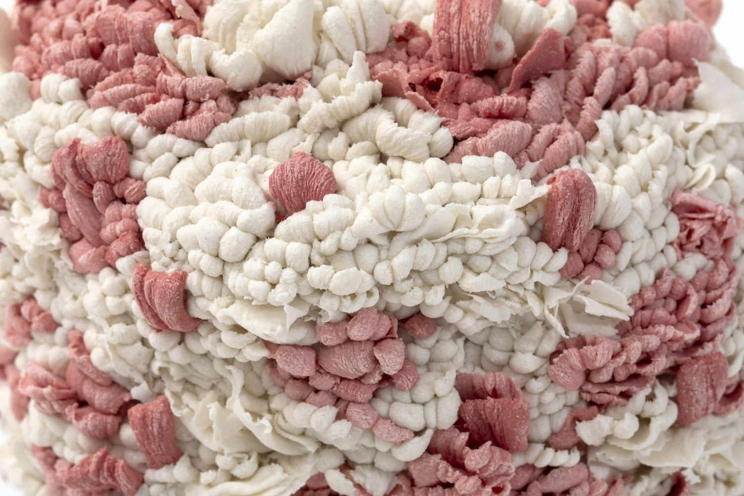 Close-up of hand-built porcelain sculpture showing densely layered  pink and white intricate surface detail. 