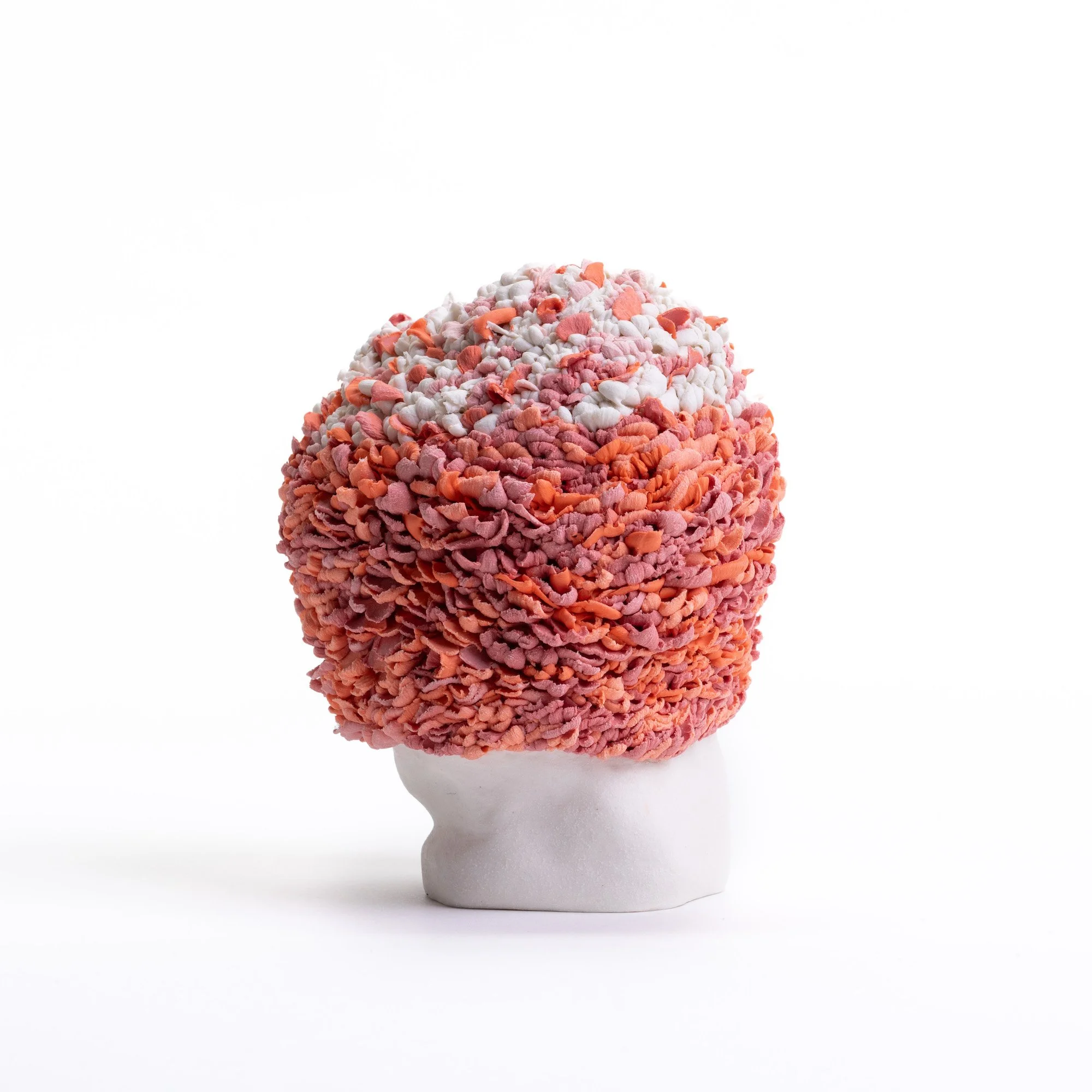 Hand-built porcelain sculpture with a rounded upright form and densely textured pink, white and orange clustered surface on a white background.