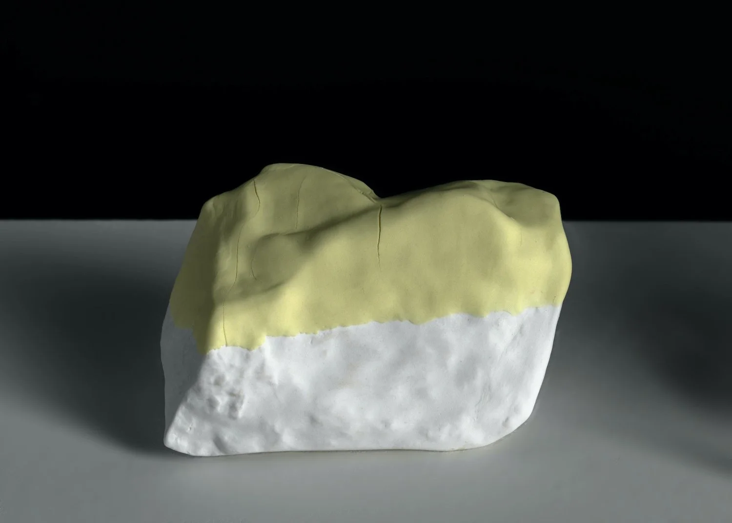 Bone china sculpture cast from a stone collected during research in Japan. A band of yellow contrasts with the textured white surface, transforming a found object into an abstract form.