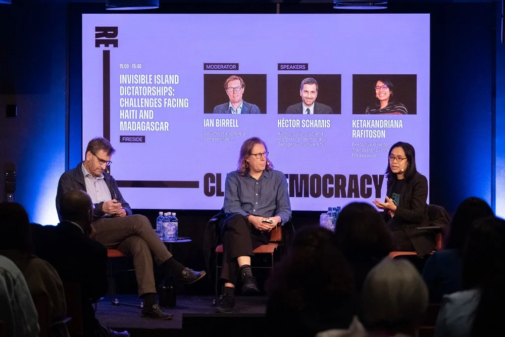 Panel discussion on challenges facing Haiti and Madagascar, featuring three speakers on stage with a presentation screen displaying their names and roles.