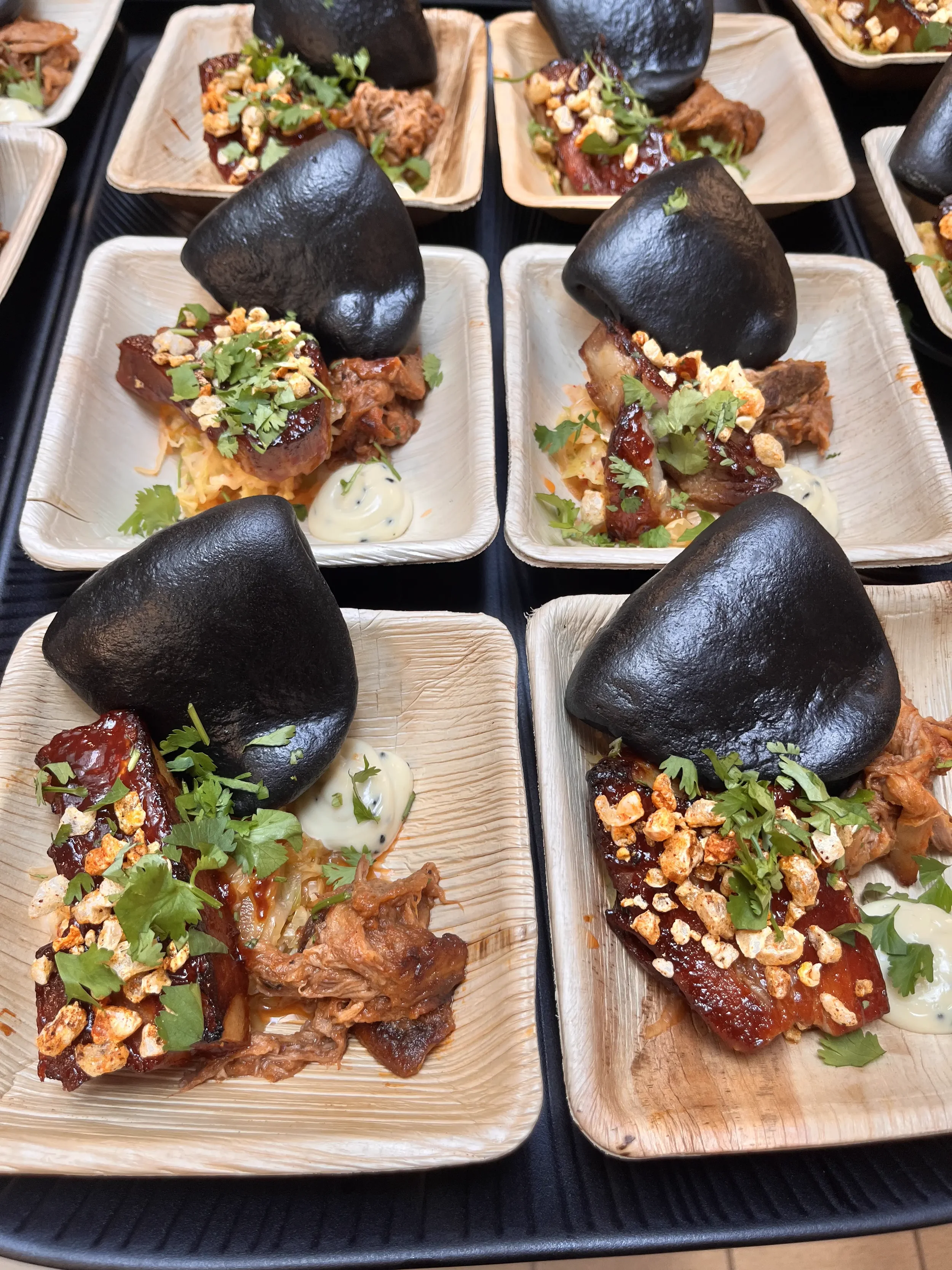 Nærbilde av flere små tapasretter med pulled pork, grønnsaker, koriander, BBQ-saus, sortir på små tallerkener.