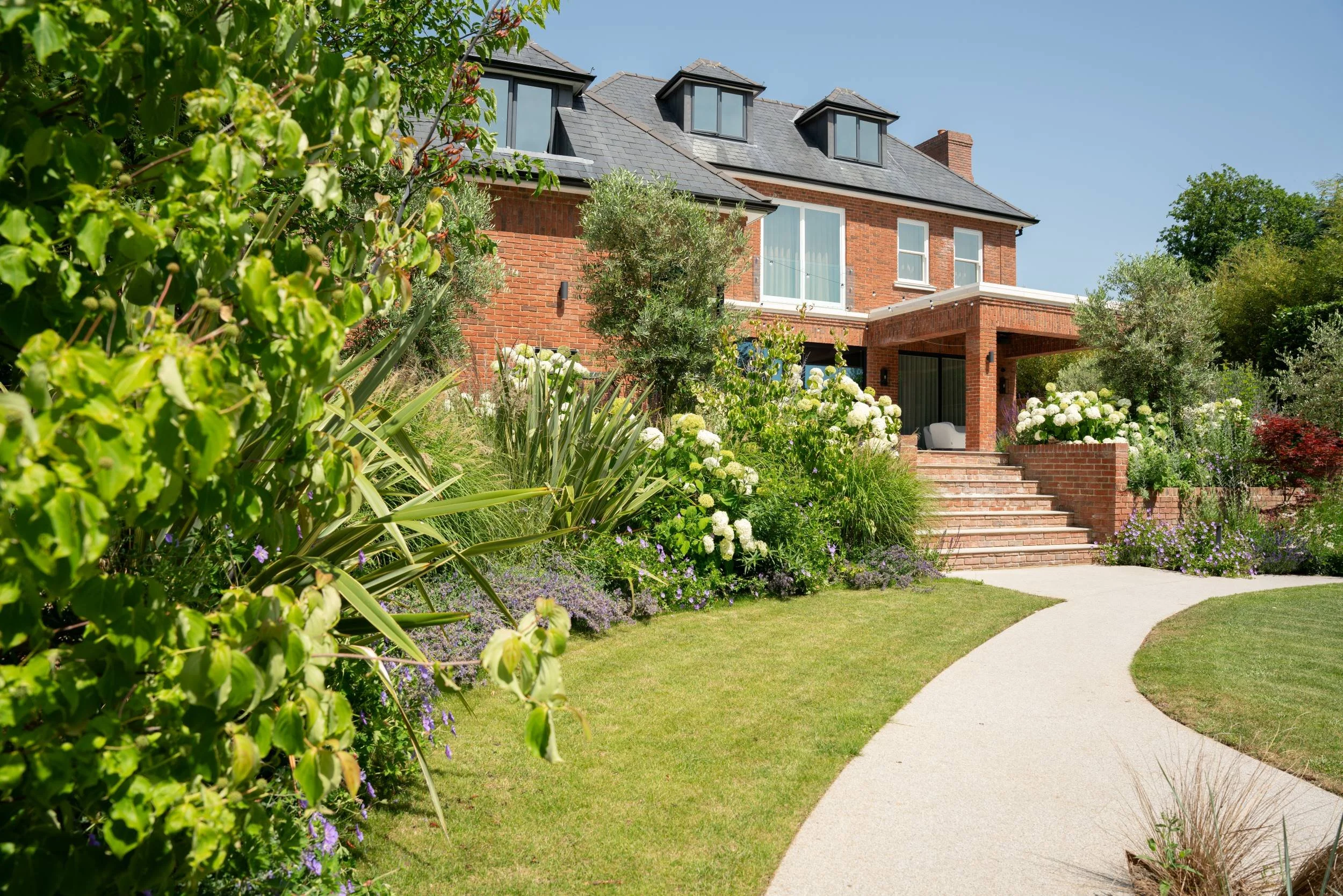 House, raised beds, curved path and lawn of a Cobham garden after planting by Paul Studholme