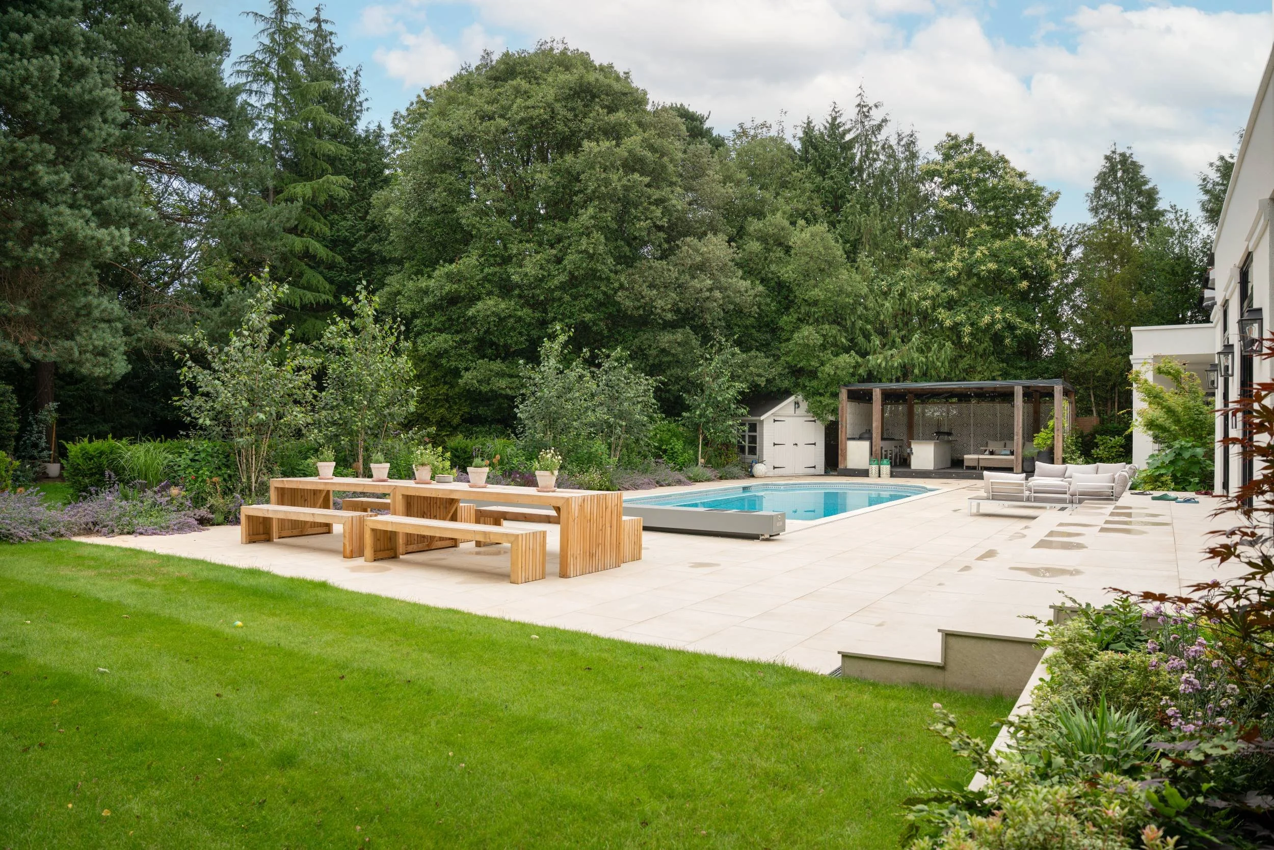Paved social area with a long table beside the pool in a family garden in Weybridge designed by Paul Studholme