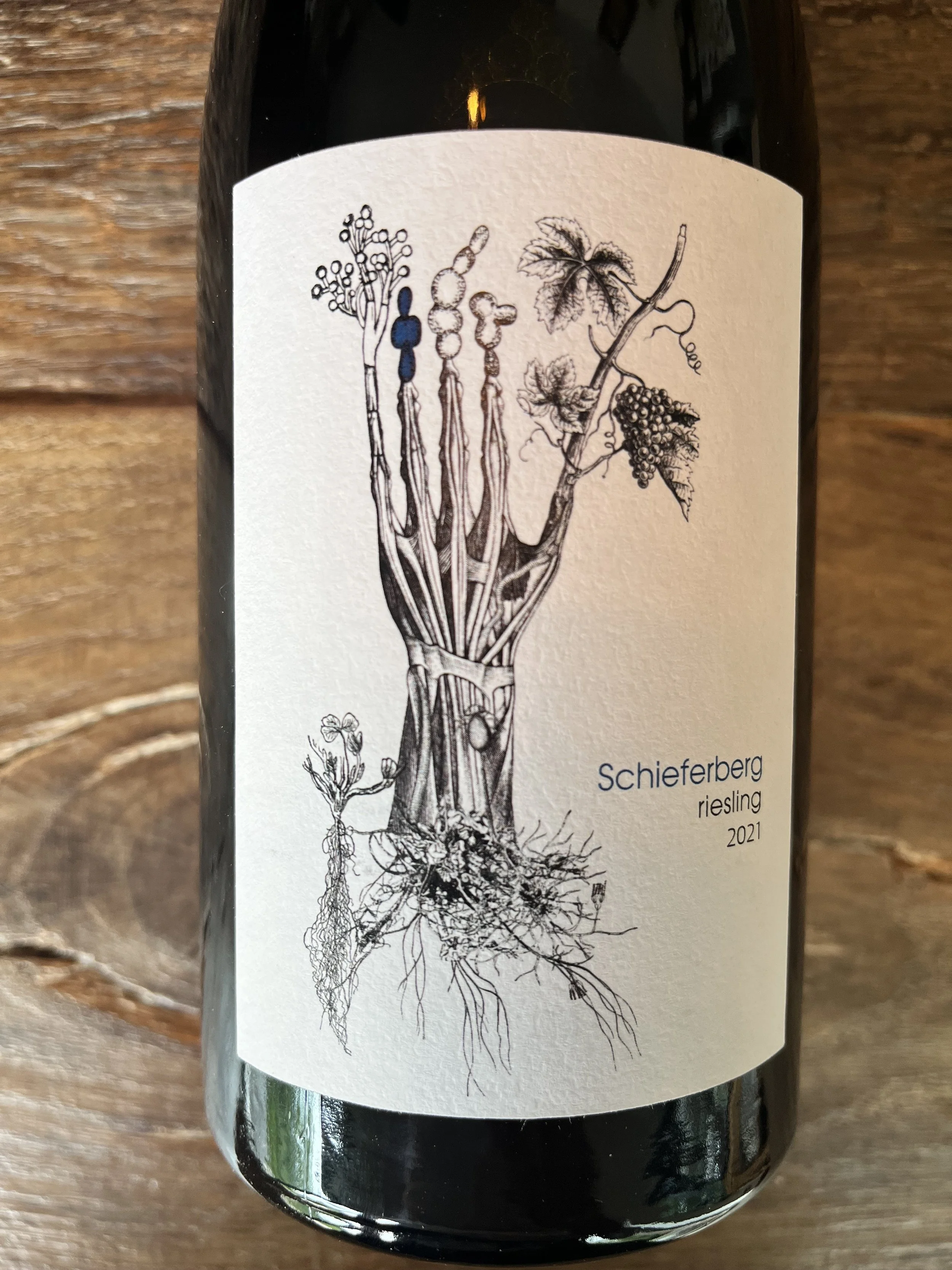 Wijnfles met een zwart-wit illustratie van druiven en wijnstokken, en de tekst 'Schieferberg riesling 2021'.