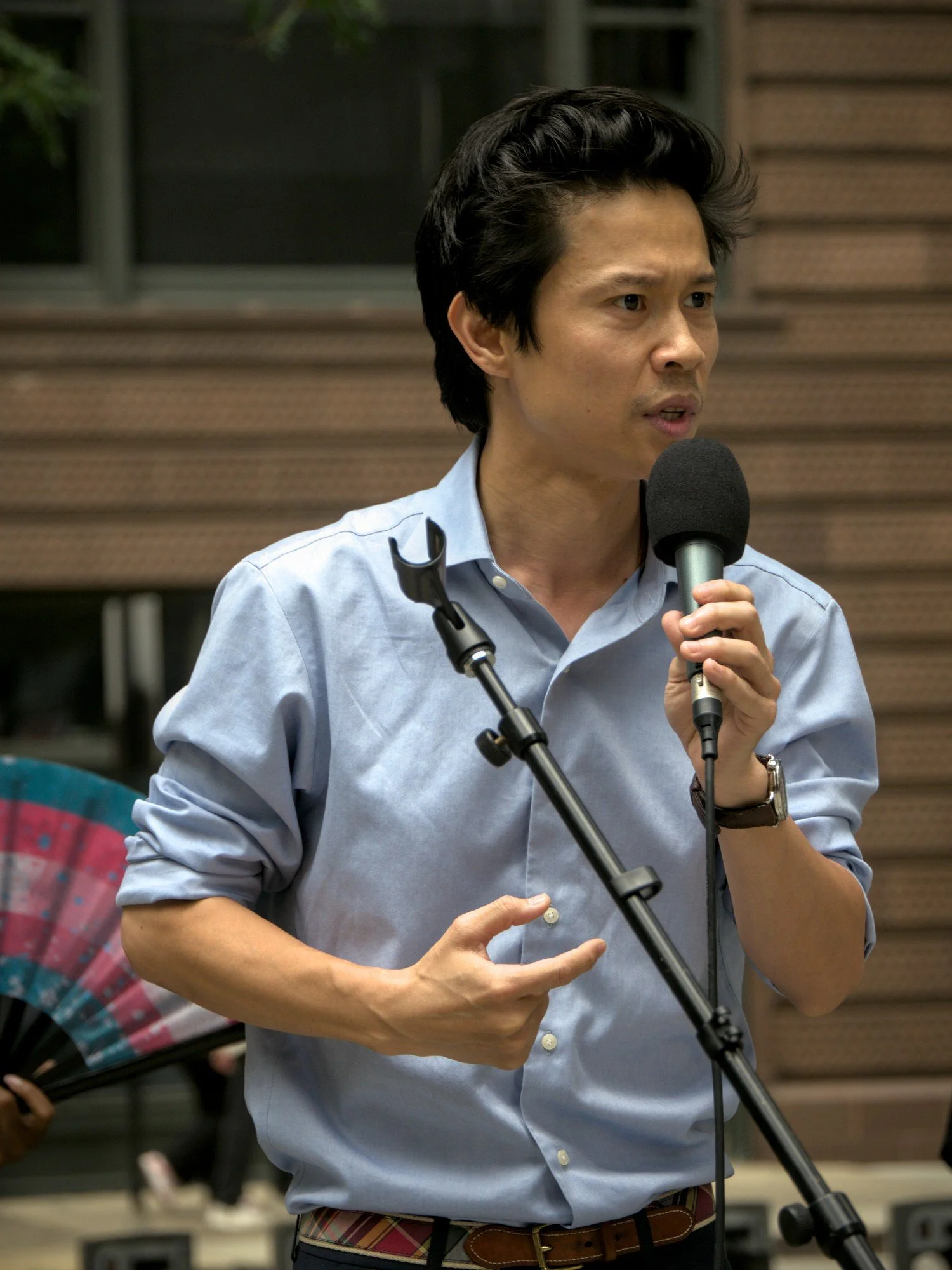   State Representative Hoan Huynh, wearing a blue button-up and jeans) speaks to the crowd into a microphone.  
