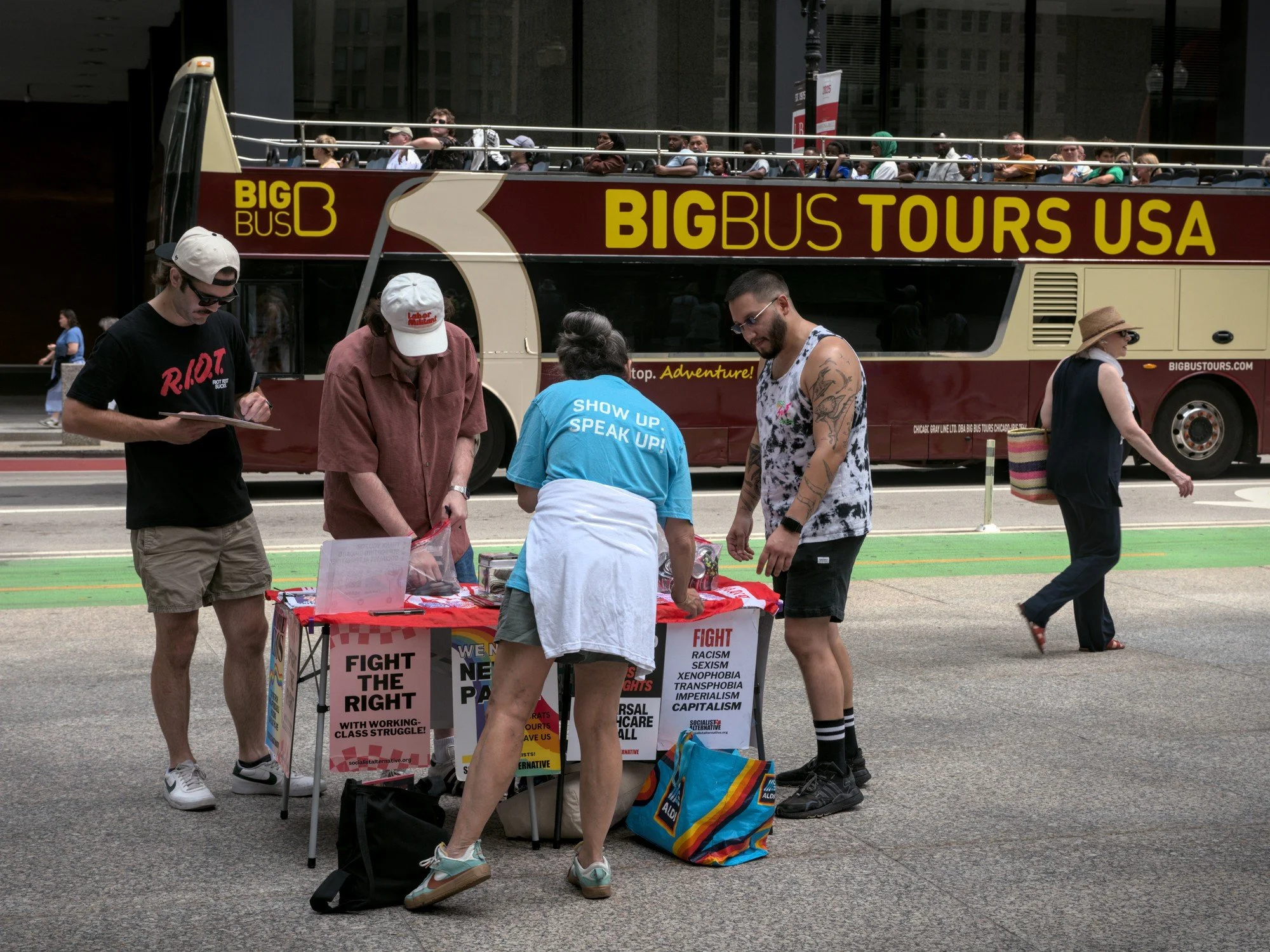   Another protest group, Socialist Alternative, hands out buttons and flyers at their table on the edge of the plaza, as a gigantic tour bus passes by.  