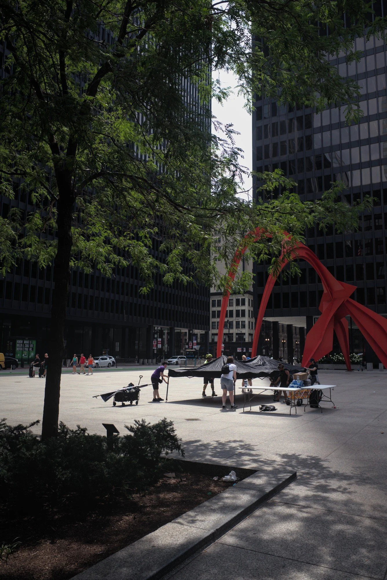   A long shot of the Flamingo statue in Federal Plaza, with the Trans Up Front crew setting up a festival tent in front of it.  