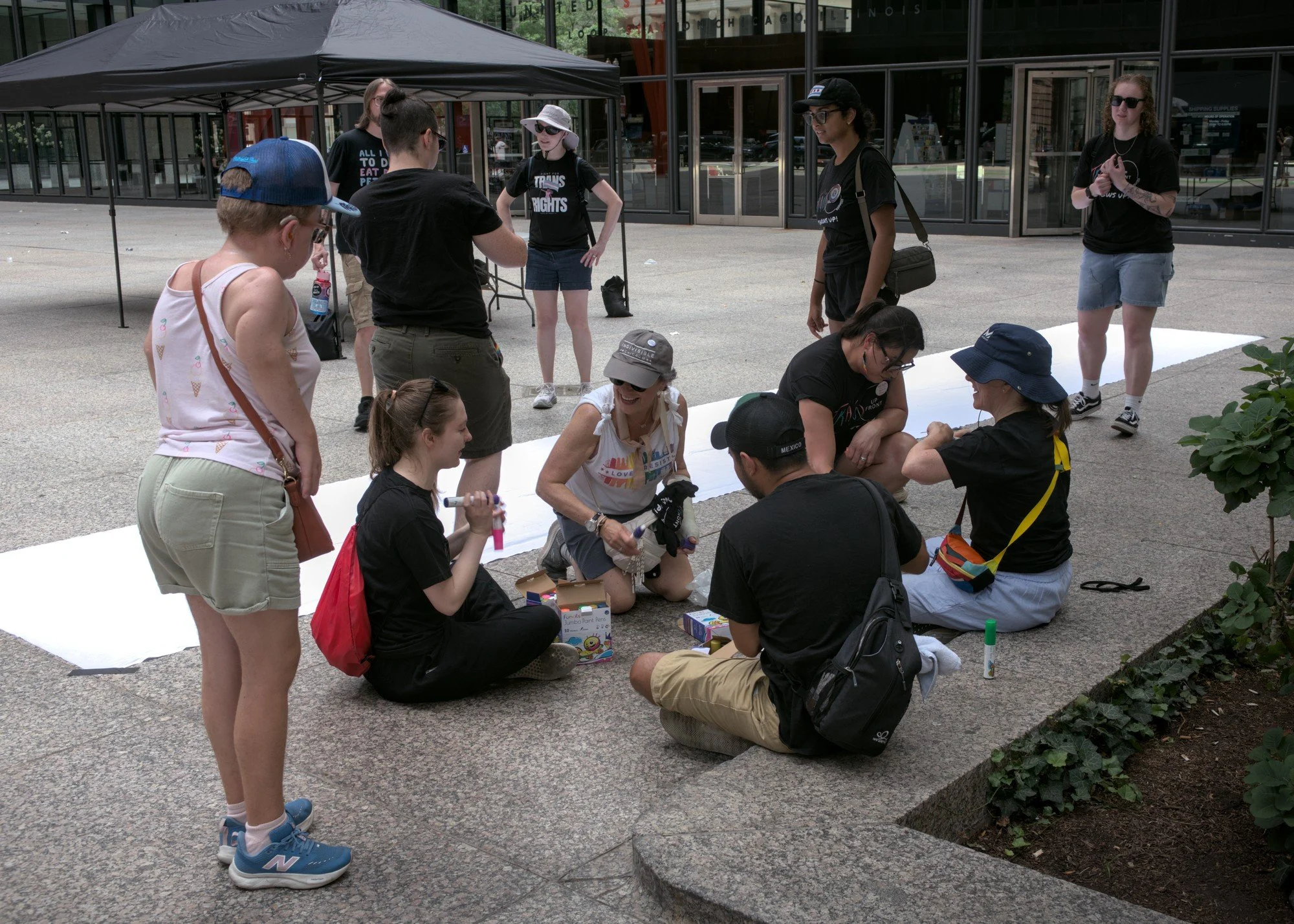   A group of smiling attendees and volunteers gather around a marker box and a gigantic white banner.  
