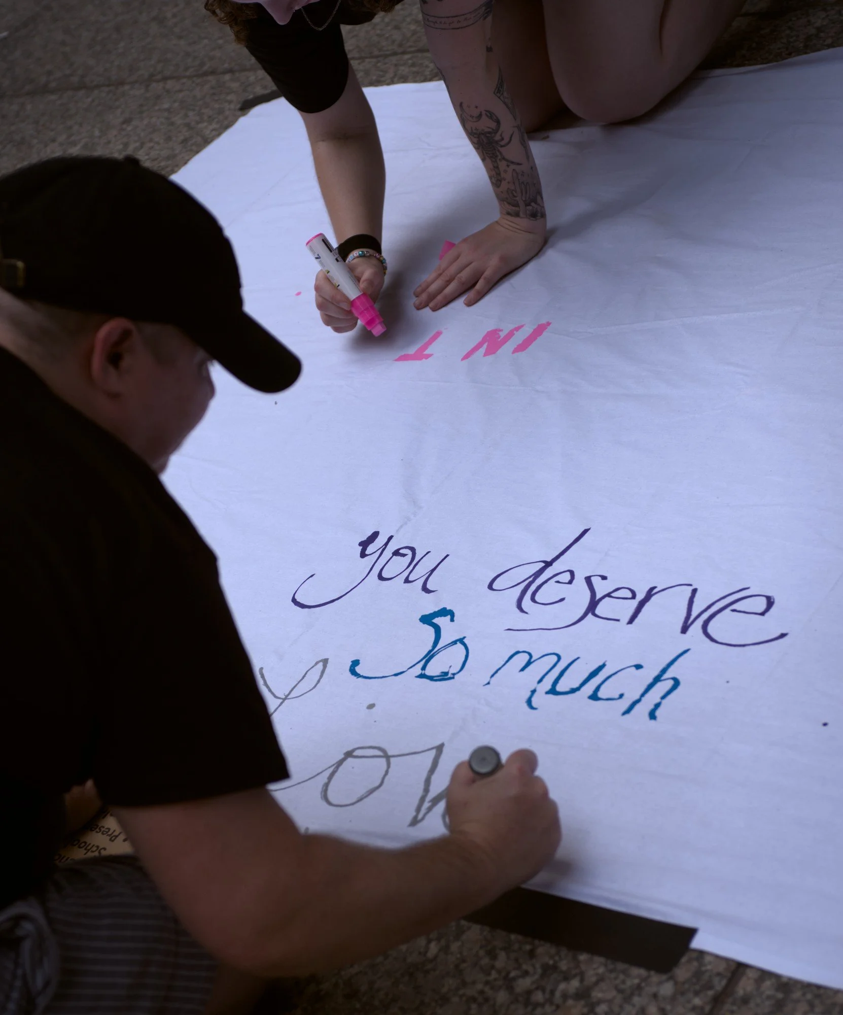   Two figures draw on the art banner, with the person closest to the viewer writing the words 