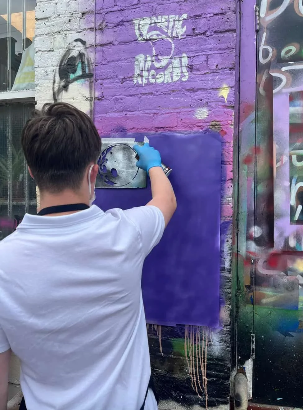 A young person stood spray painting a stencil of the moon onto paper sprayed purple..