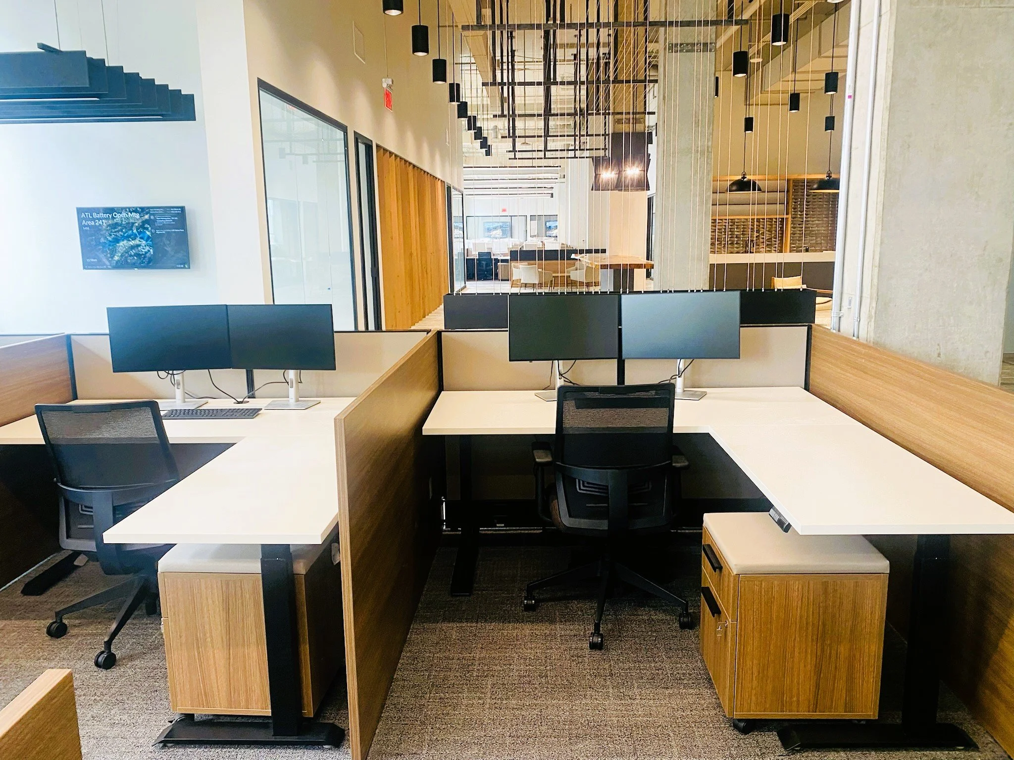 Modern office workspace with four computer monitors, black chairs, and wooden dividers.