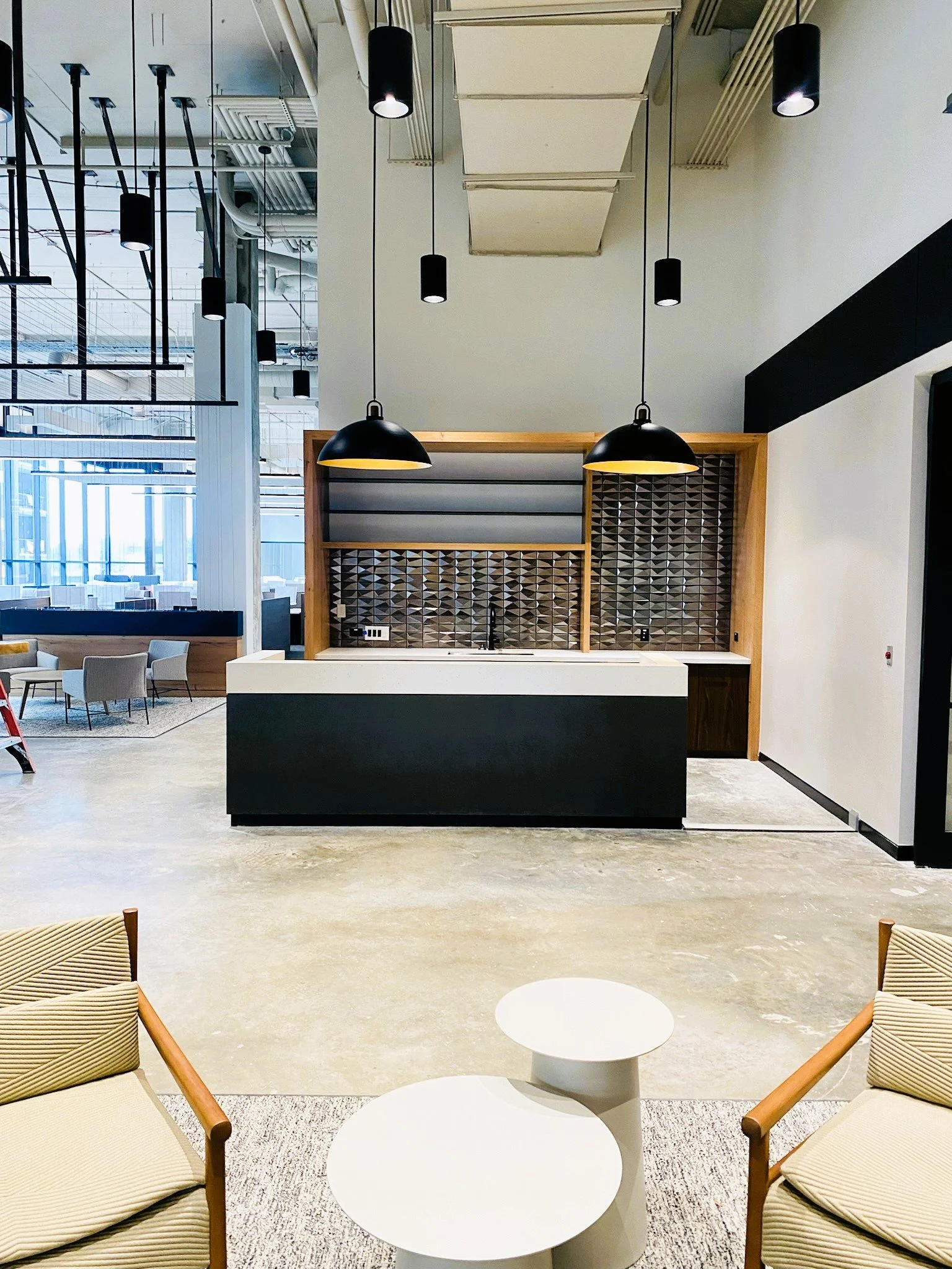 Modern lounge area with beige chairs, a white coffee table, and a black and white bar or counter with black pendant lights hanging above.